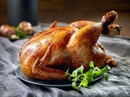 Un pavo asado está sentado en un plato sobre una mesa.