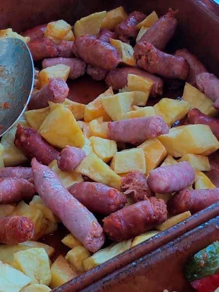 Un tazón de salchichas y patatas con una cuchara dentro.