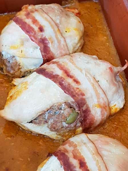Un primer plano de pollo envuelto en tocino en una sartén.