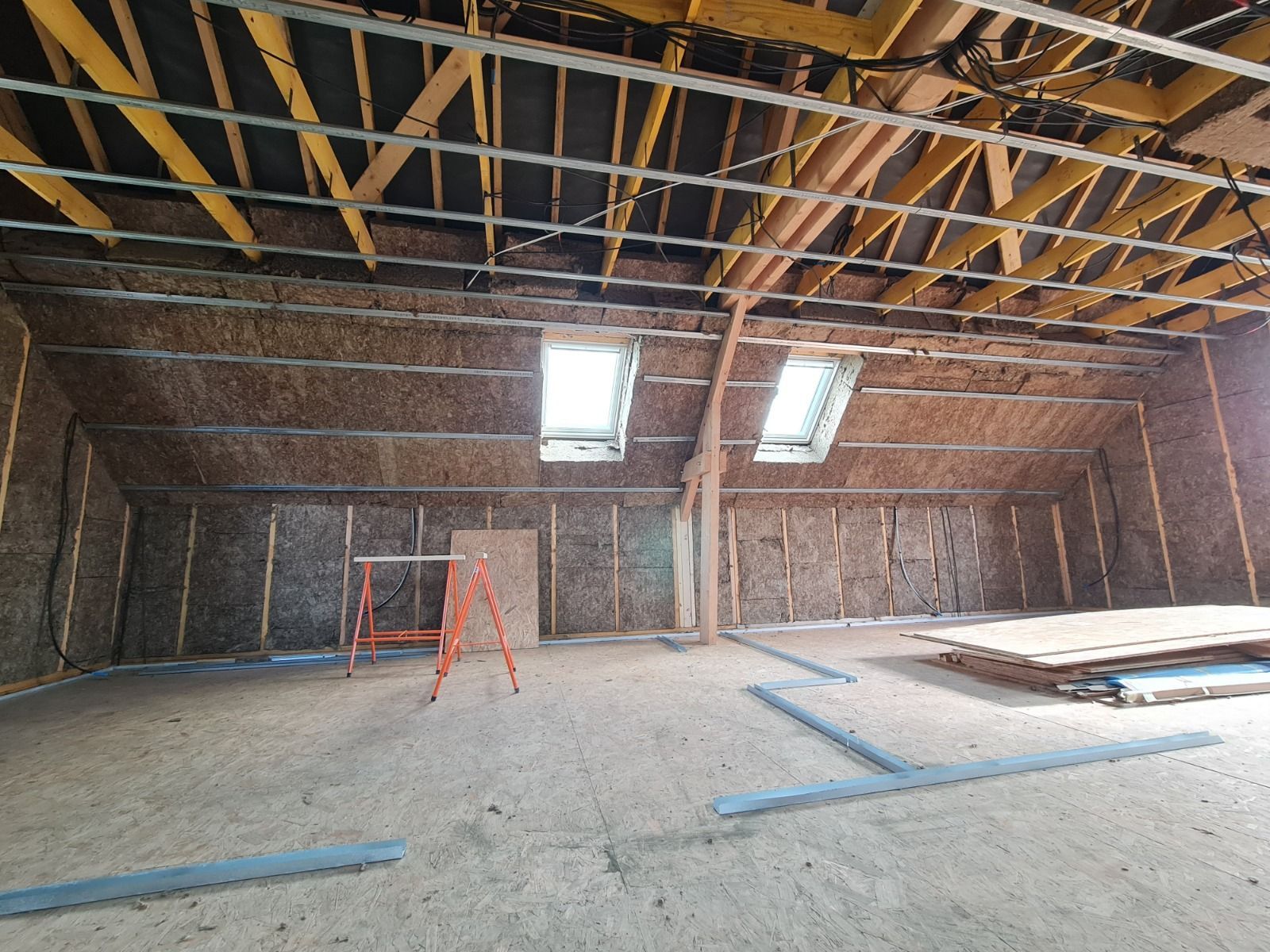 Chambre avec parquet, lit recouvert d'un couvre-lit beige, étagères et bureau intégrés et murs blancs.