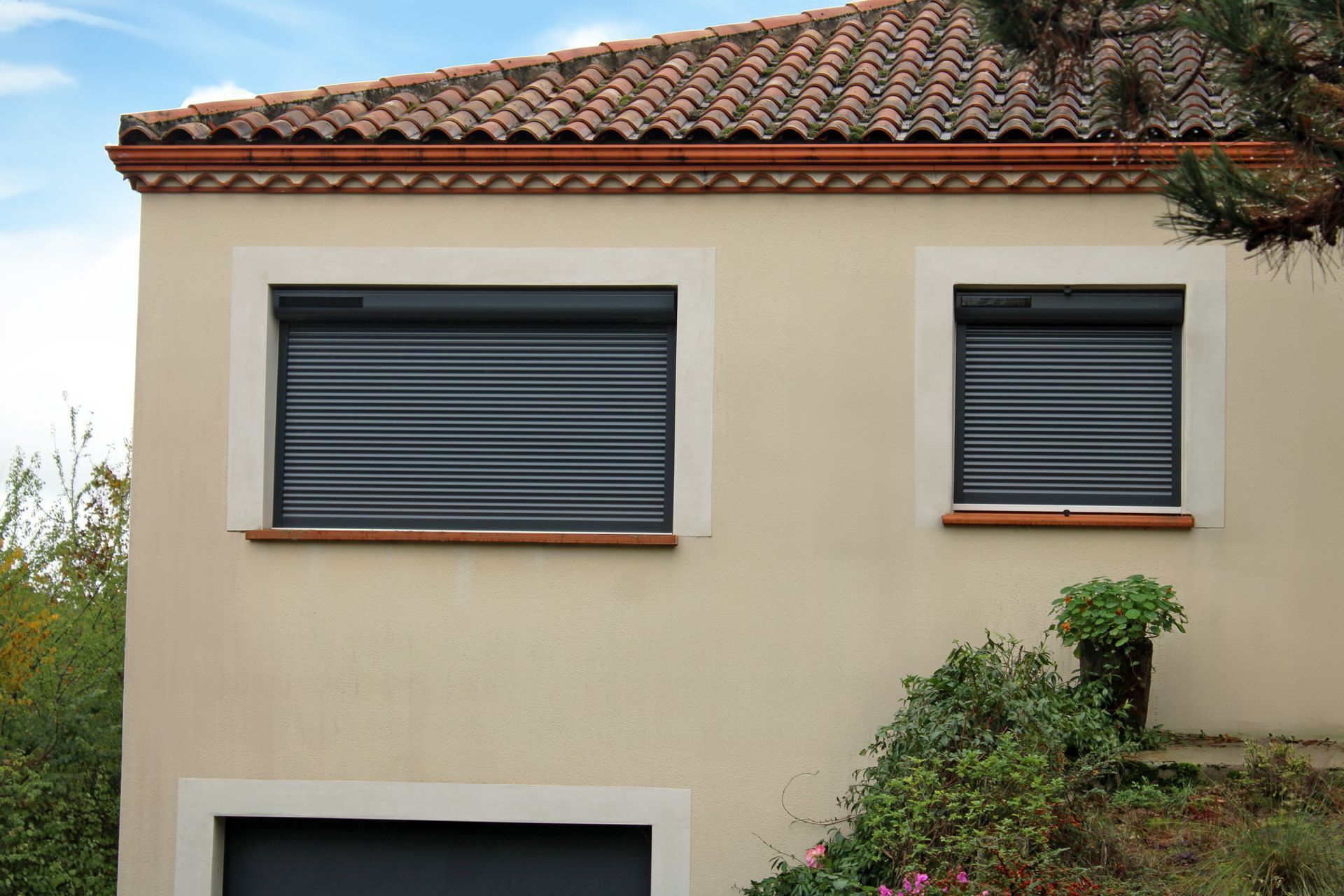 Maison à l'extérieur beige avec deux fenêtres recouvertes de volets roulants gris fermés.