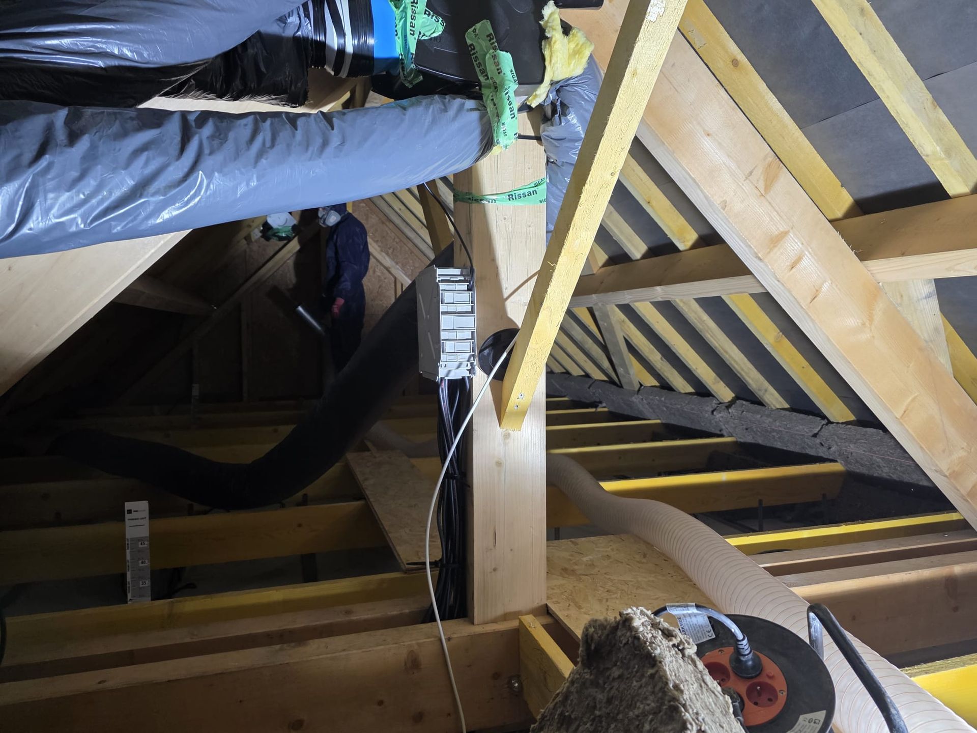 Intérieur du grenier avec isolation, ventilation et une personne près d'une poutre porteuse.