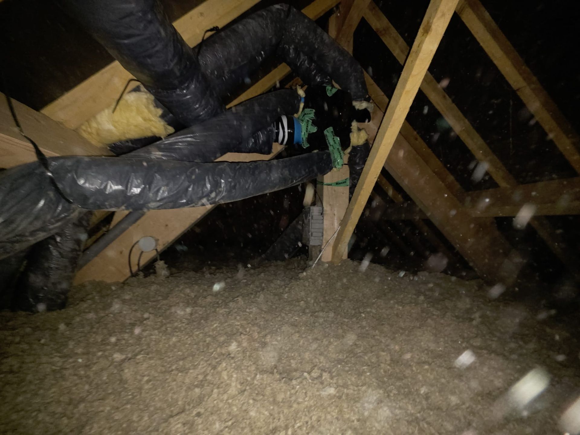 Intérieur du grenier avec isolation, conduits d'aération et charpente en bois.