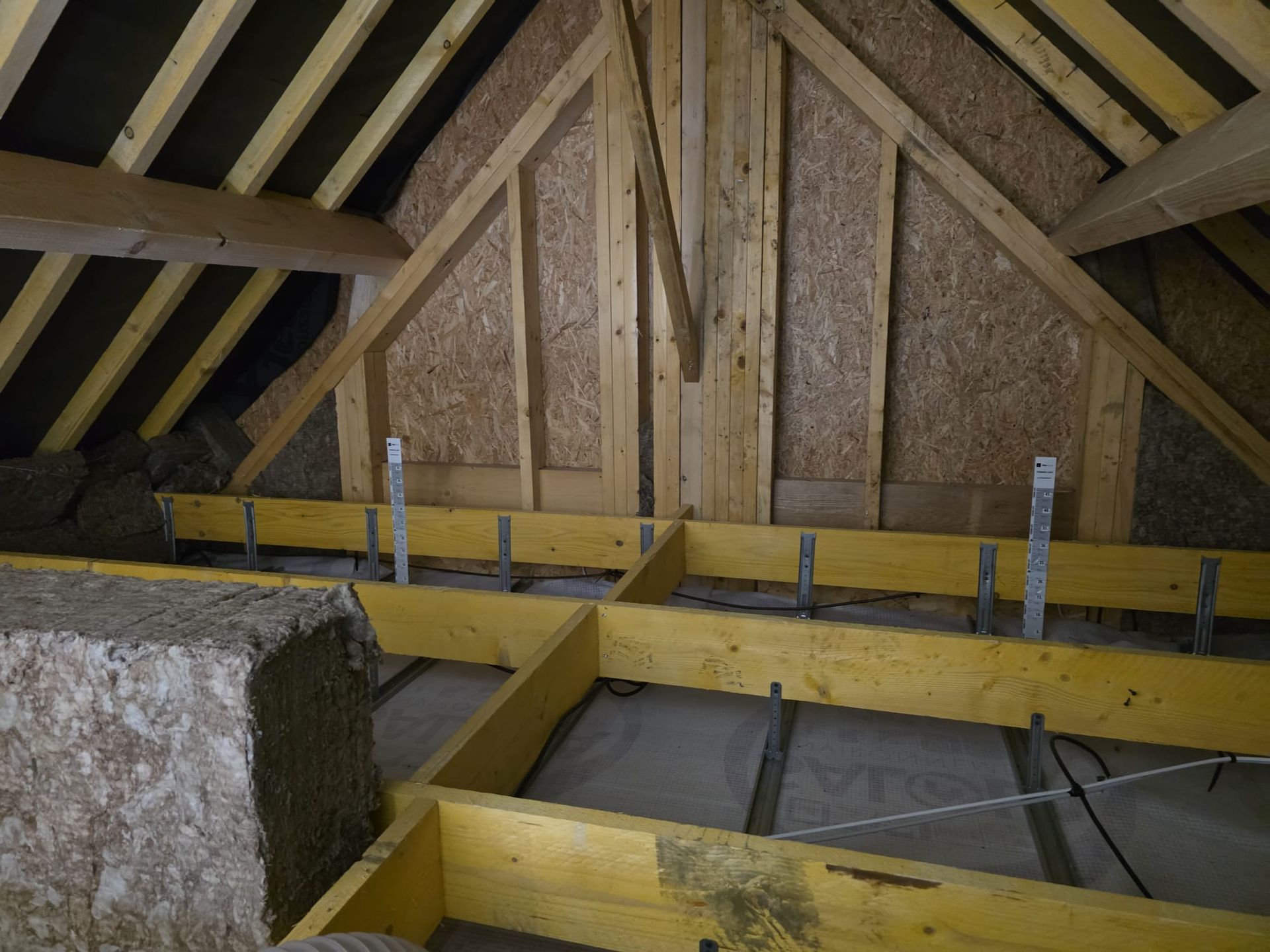 Combles aménagés avec charpente en bois, isolation et plancher non fini.