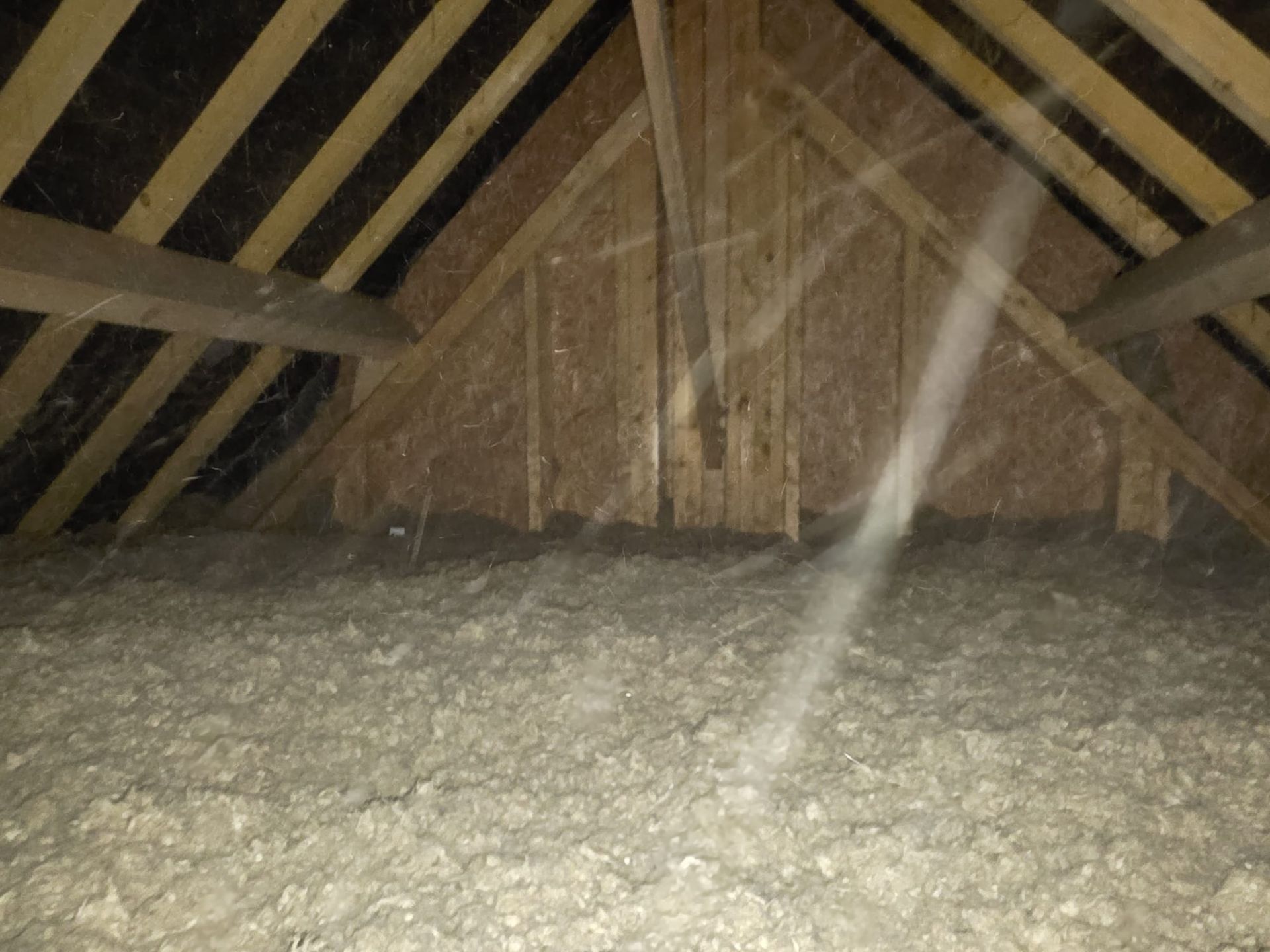 Intérieur du grenier avec isolation, poutres en bois et un faisceau lumineux ou des particules de poussière.