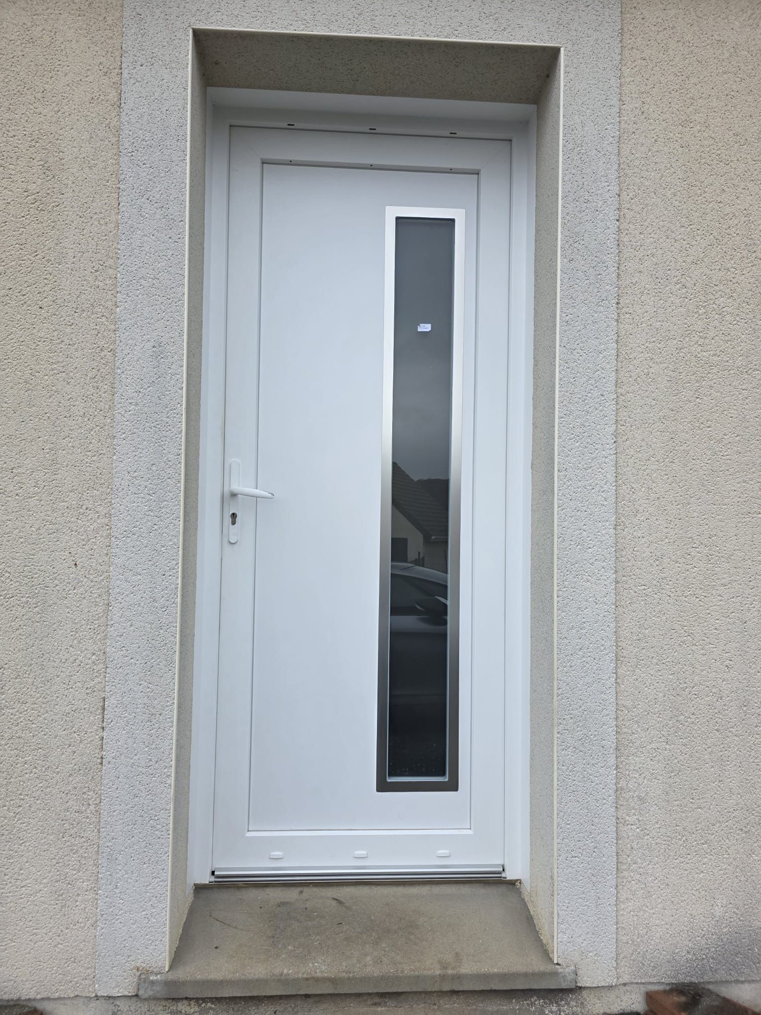 Porte d'entrée blanche avec un panneau de verre vertical, encadré d'un cadre beige clair.
