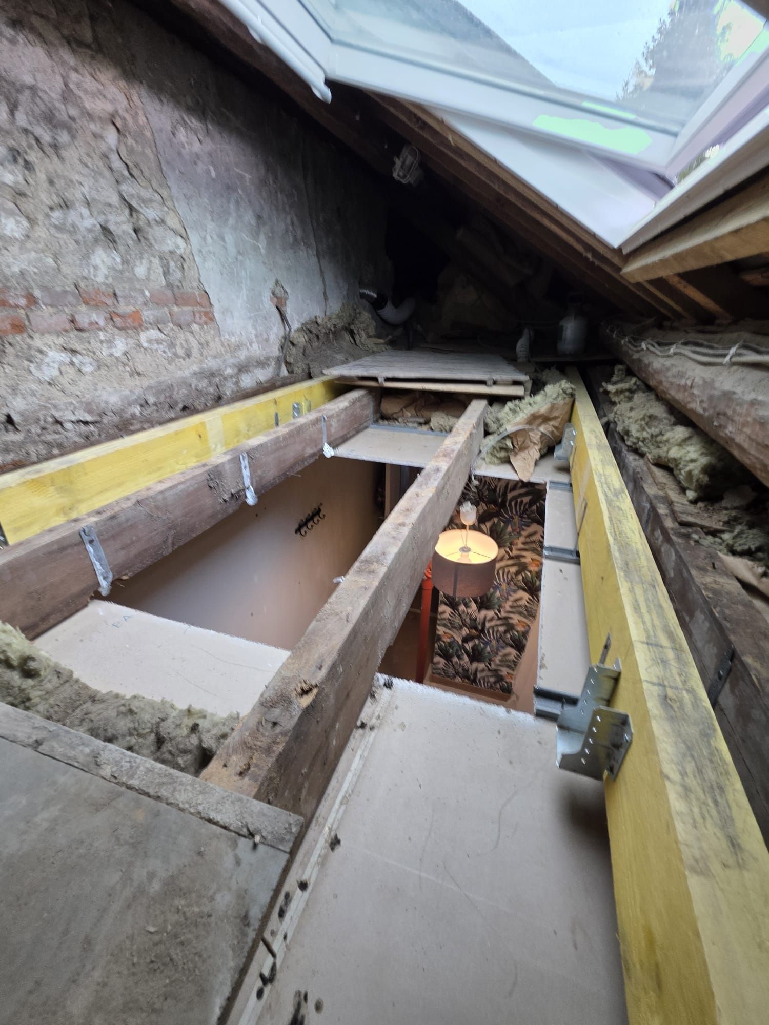 Rénovation des combles en cours avec poutres apparentes, isolation et puits de lumière.