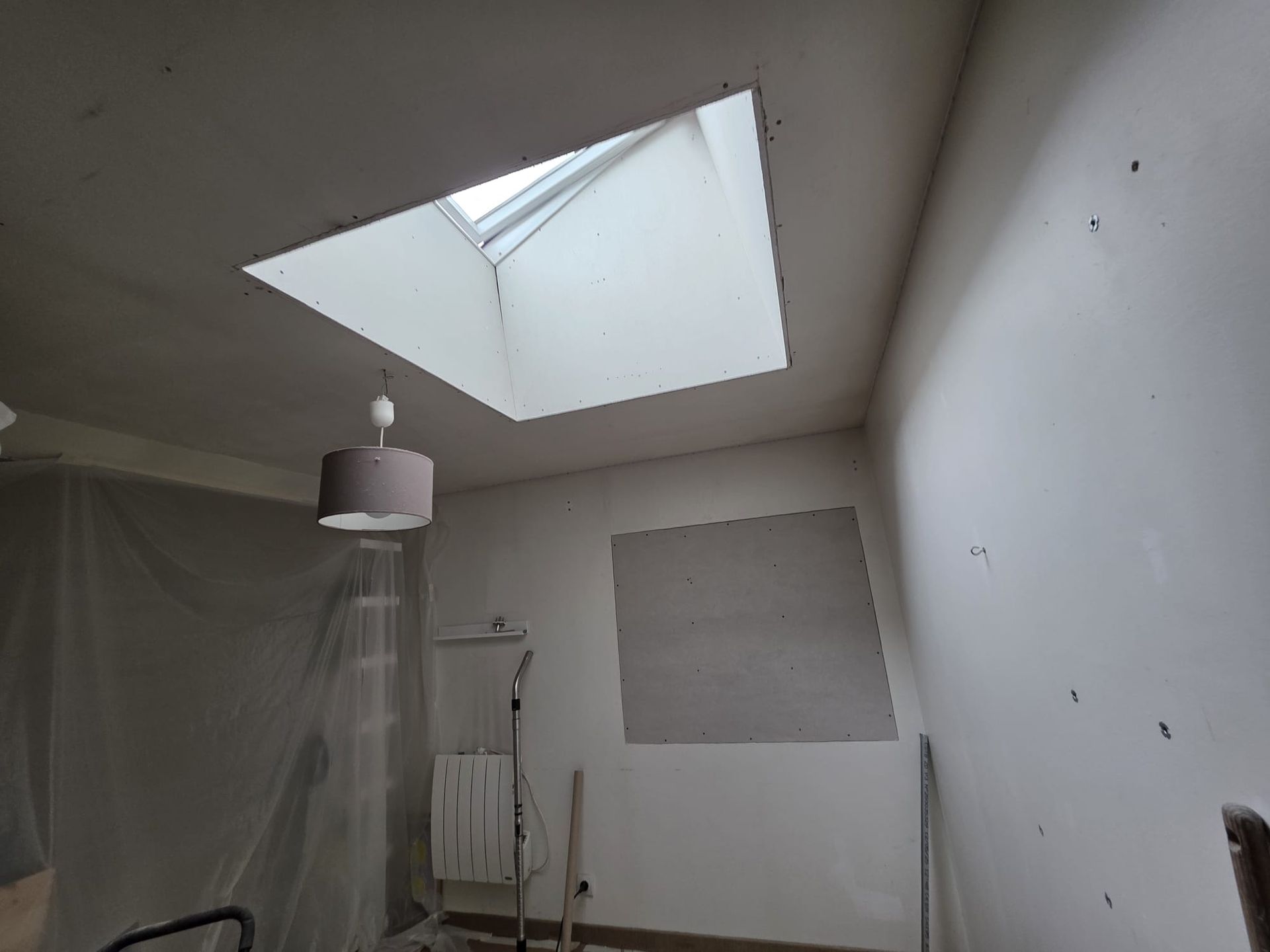 Intérieur d'une pièce avec un puits de lumière, une suspension lumineuse et un mur avec une zone apparente.