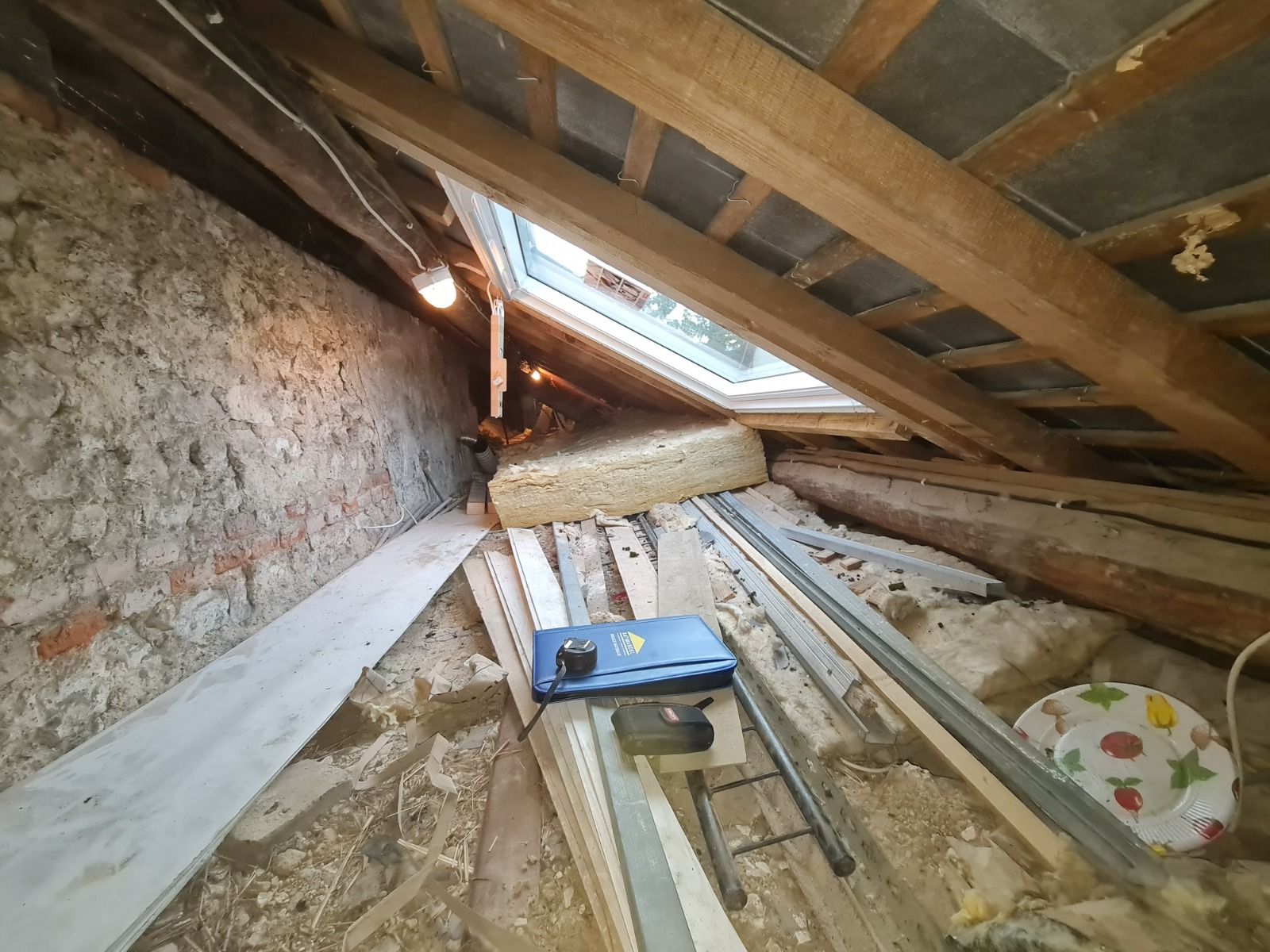 Grenier avec puits de lumière, isolation, poutres en bois et matériaux de construction.