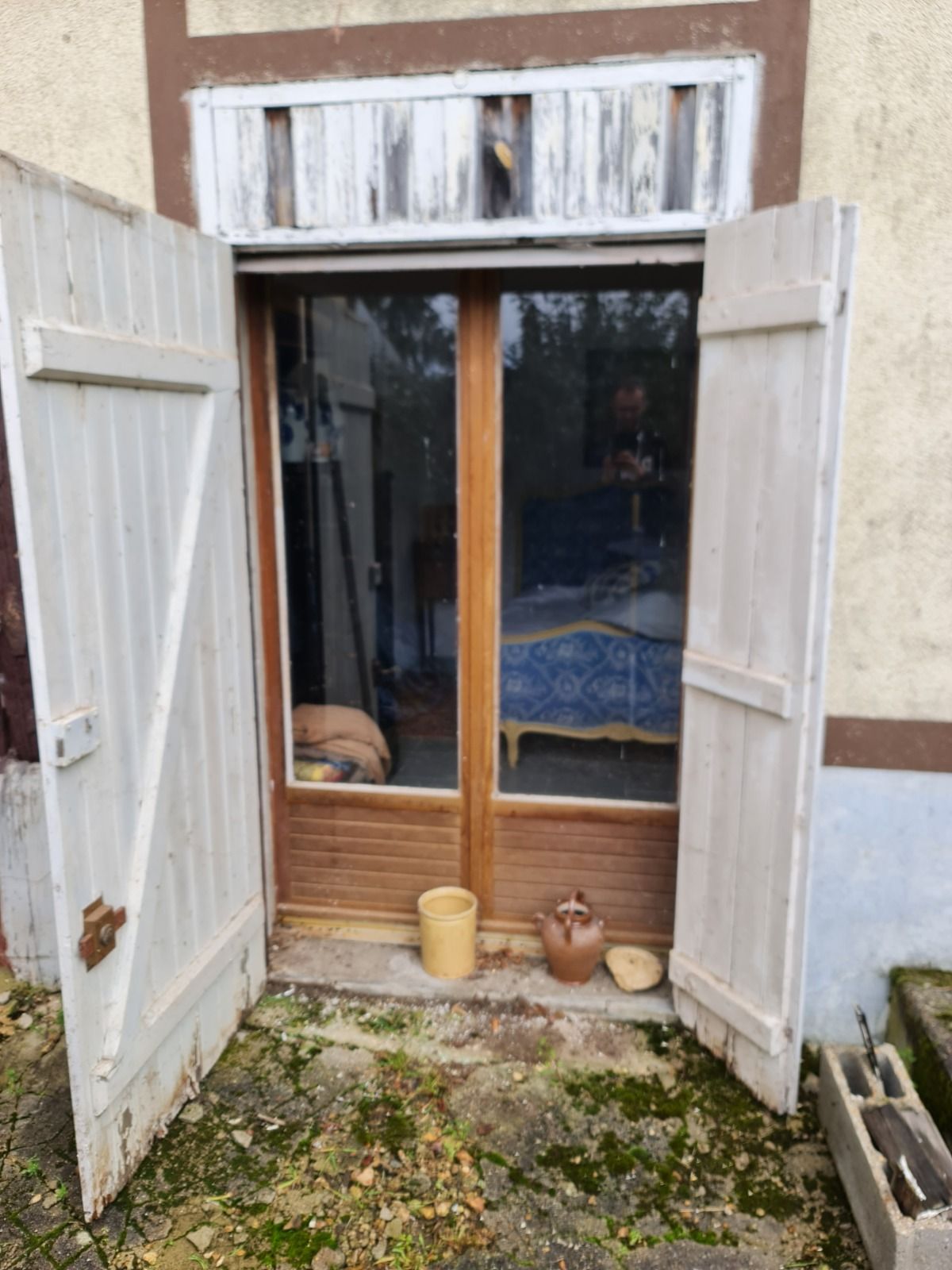 Des portes doubles à volets blancs s'ouvrent sur une pièce où l'on aperçoit un canapé et un chien.