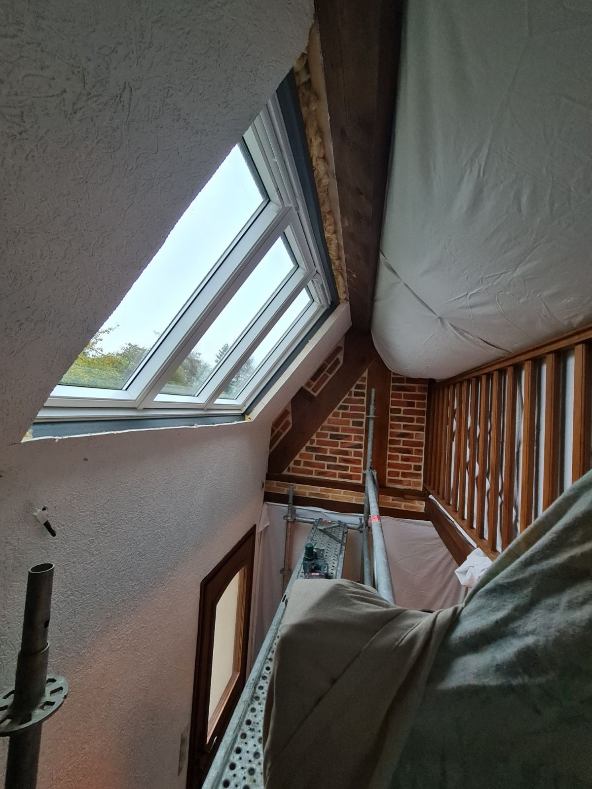 Intérieur du grenier avec puits de lumière, poutres apparentes et un mur partiellement construit.