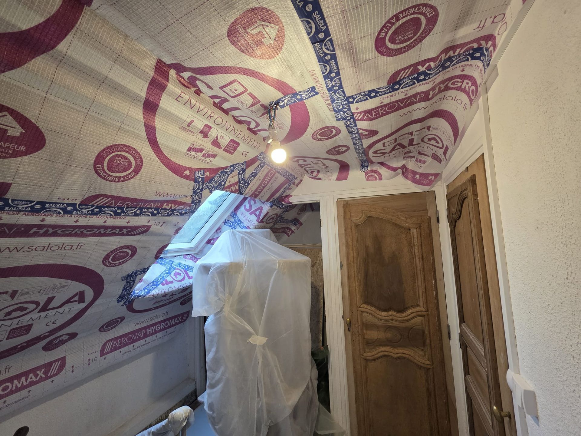 Grenier isolé, avec puits de lumière, luminaire, porte en bois et objets recouverts de plastique.