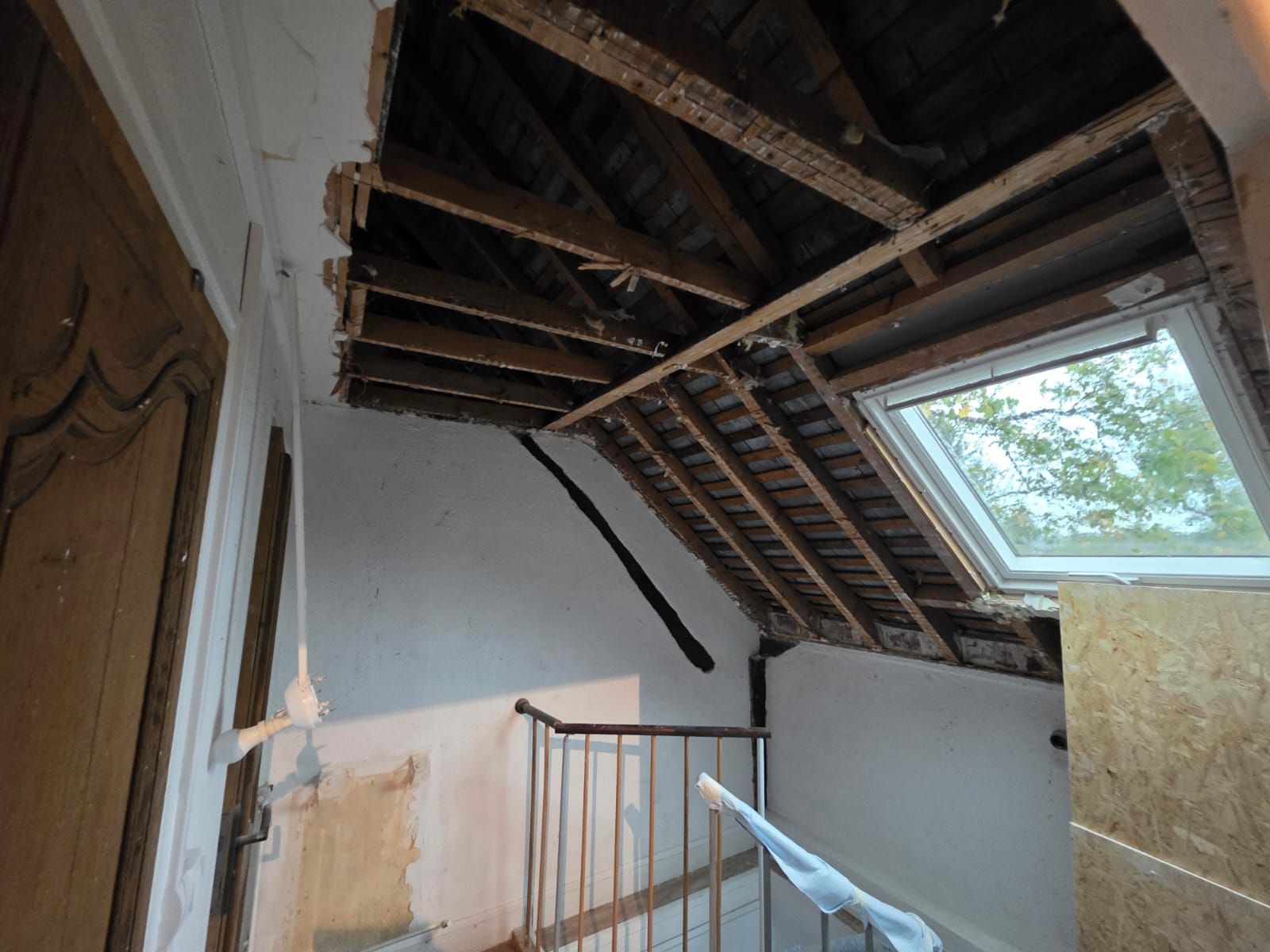 Intérieur d'une maison en rénovation, montrant les poutres apparentes, l'escalier et le puits de lumière.