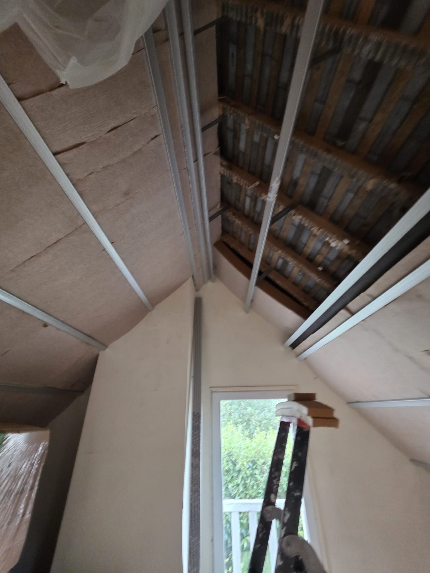 Vue intérieure d'un grenier en cours de rénovation, avec poutres apparentes, cloisons sèches et une échelle près d'une fenêtre.