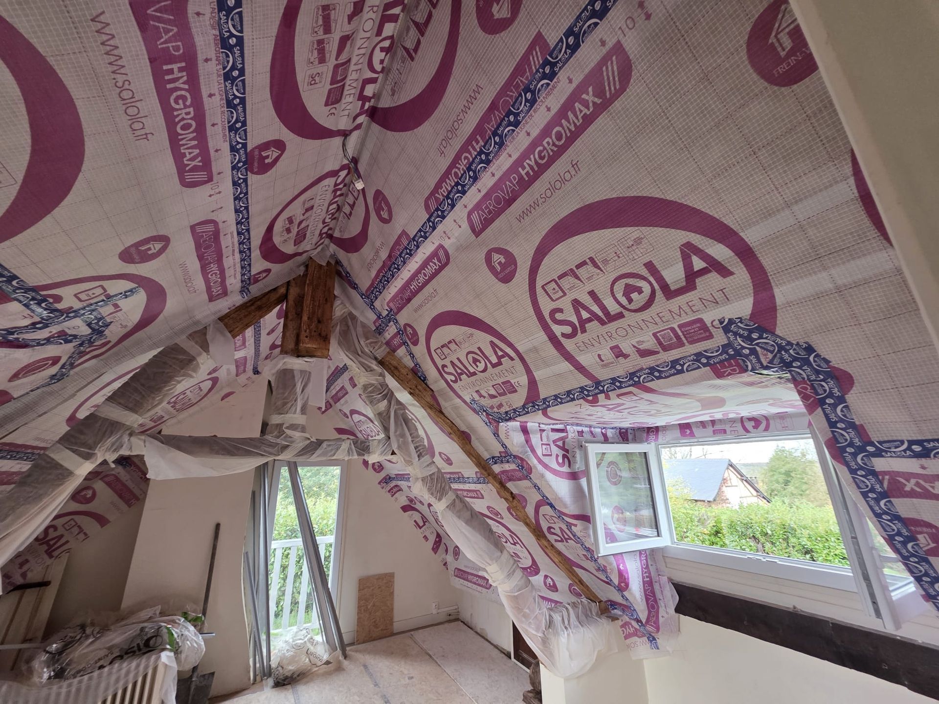 Intérieur du grenier isolé, poutres en bois et fenêtre donnant sur la verdure.