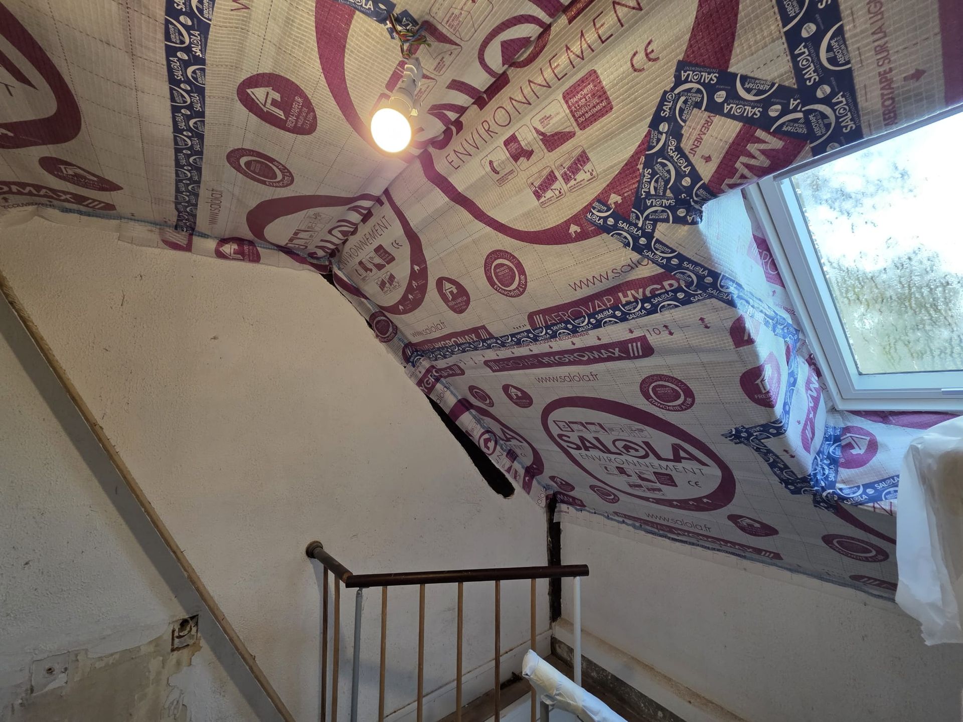 Grenier avec isolation au plafond, un escalier et une fenêtre. Un luminaire est suspendu au plafond.