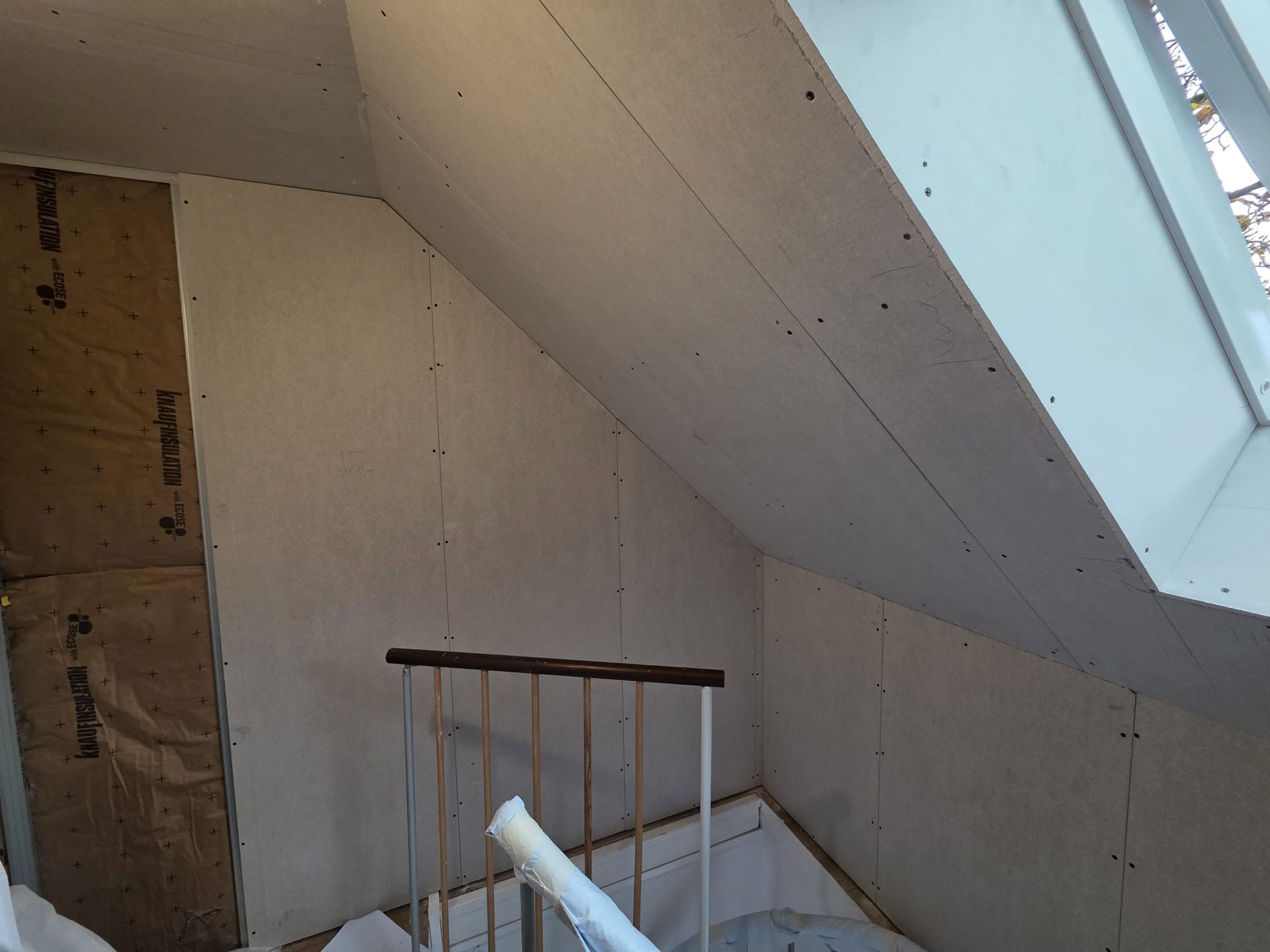 Vue intérieure d'un grenier dont les cloisons sèches sont partiellement installées ; un puits de lumière est visible.