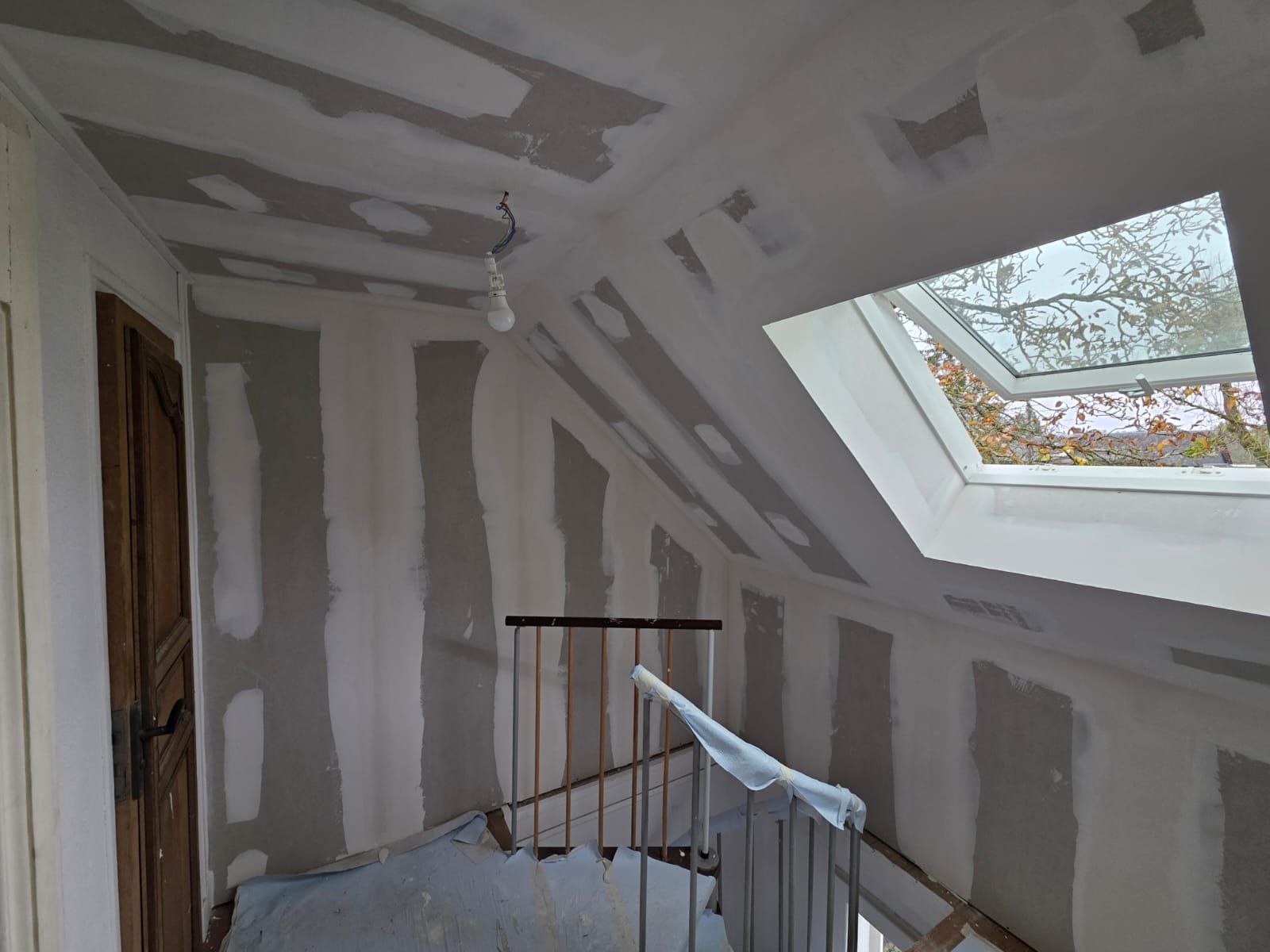 Rénovation intérieure : pose de plaques de plâtre sur les murs et le plafond ; puits de lumière visible.
