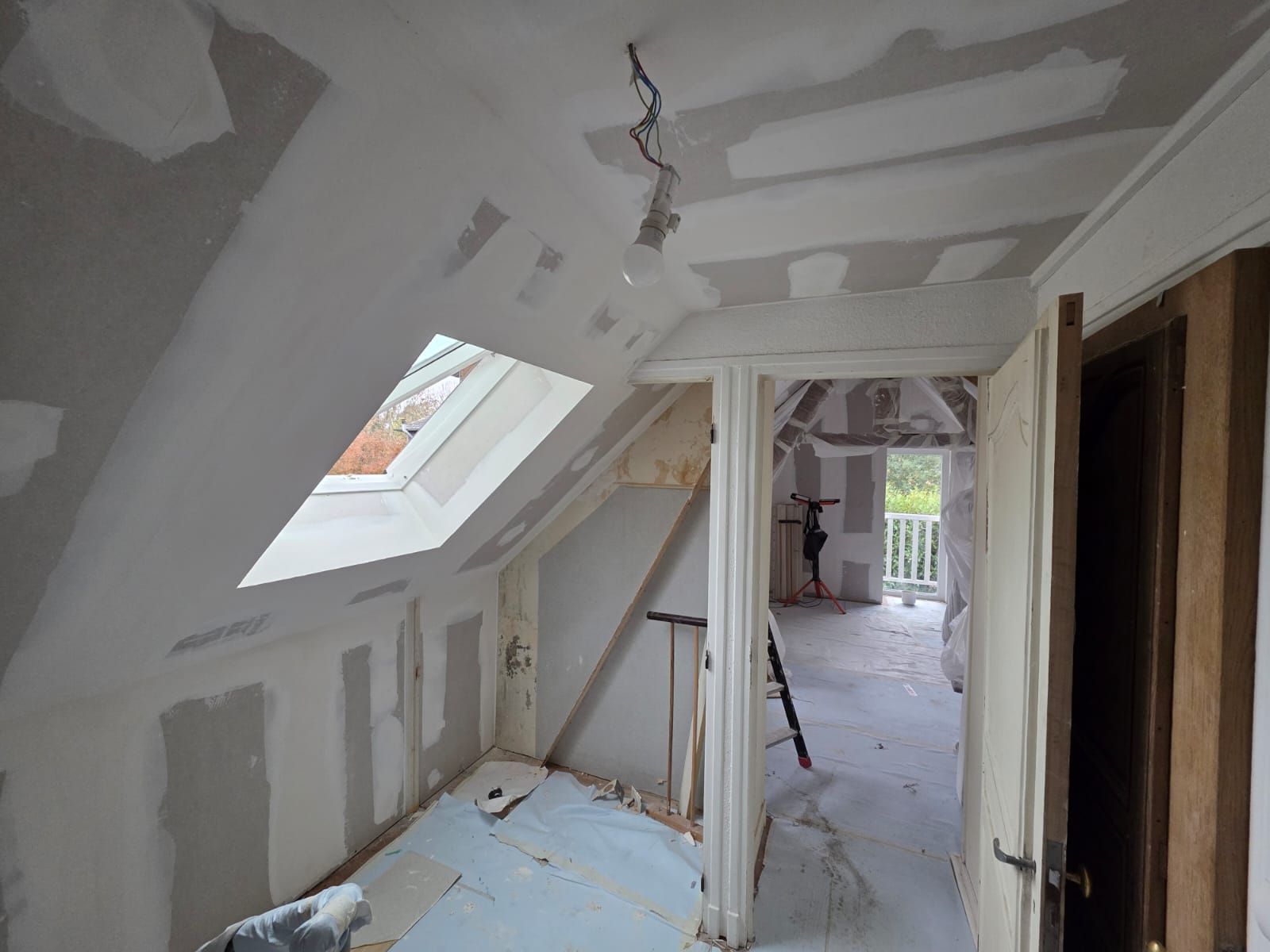 Pièce intérieure en cours d'aménagement, murs et plafond en plaques de plâtre, grandes fenêtres.