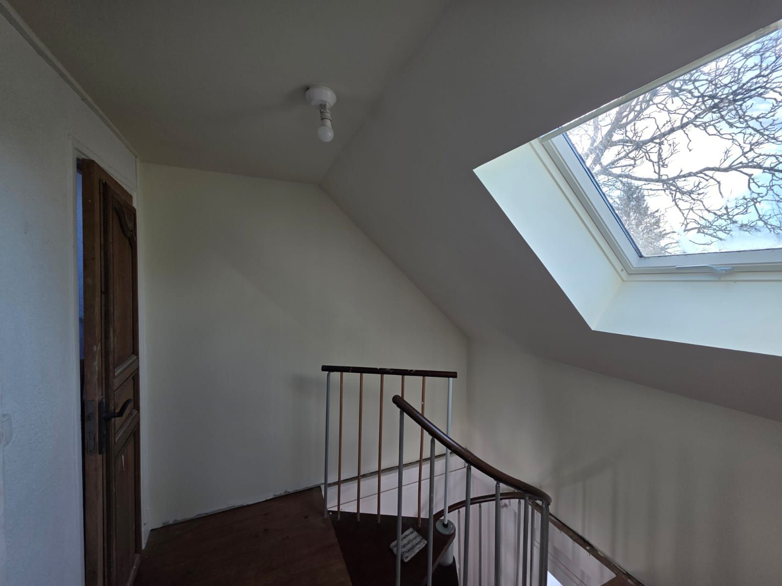 Vue intérieure d'une cage d'escalier avec un puits de lumière et une porte en bois fermée.