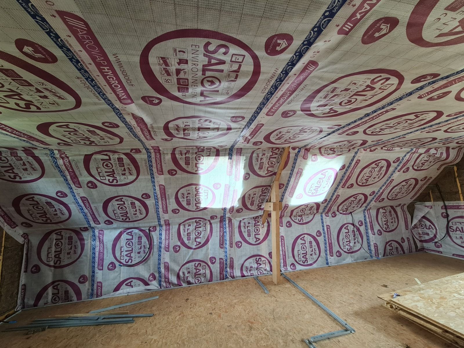 Mur intérieur en construction avec une fenêtre et des montants métalliques, non fini, laissant apparaître l'isolation.