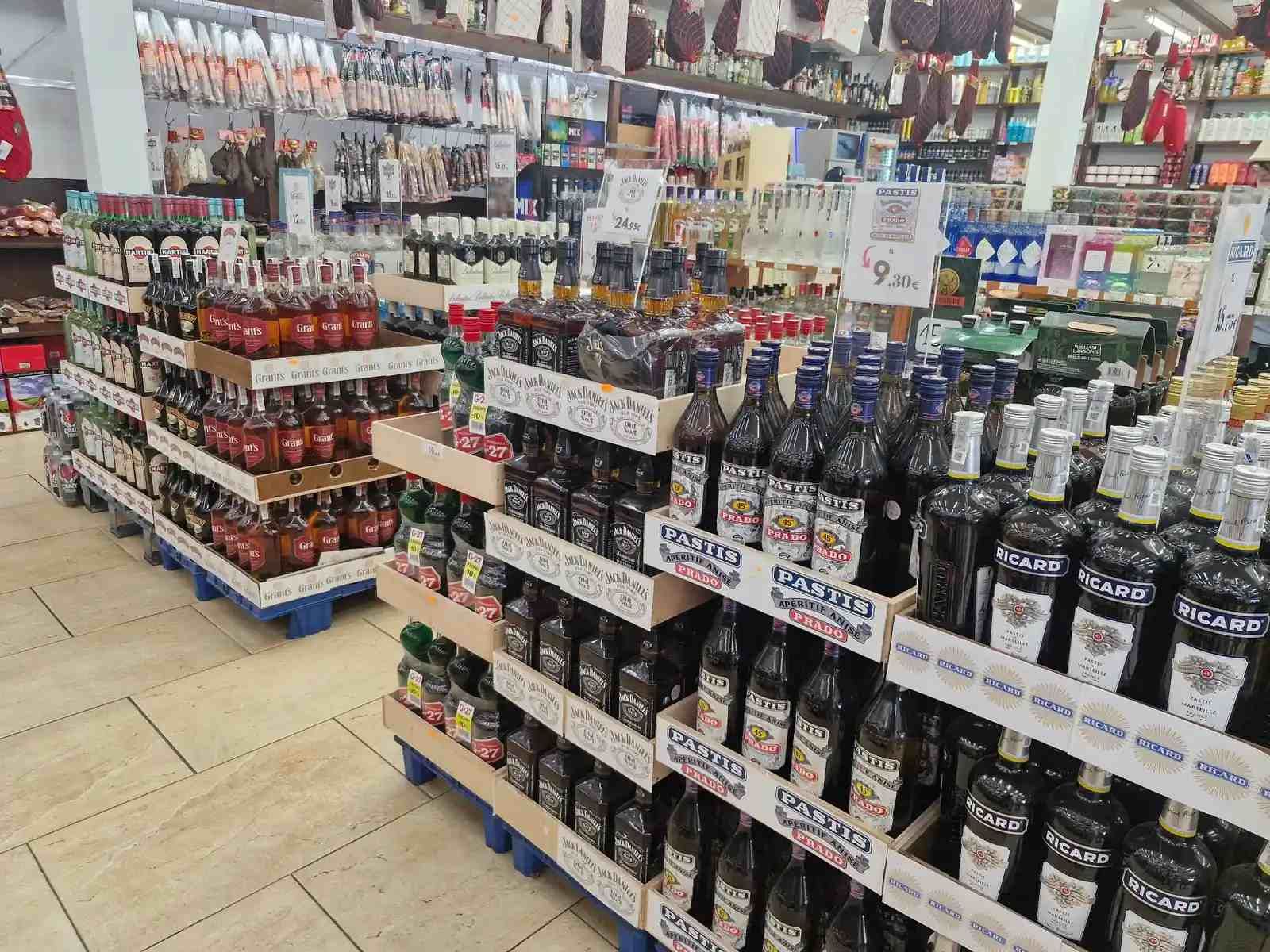 Estanterías repletas de botellas de licor en una tienda bien iluminada. Botellas marrones, verdes y azules se exhiben sobre palés.