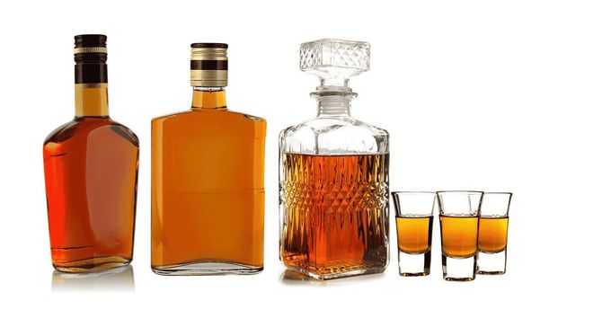 Botellas de licor ámbar con tres vasos de chupito.
