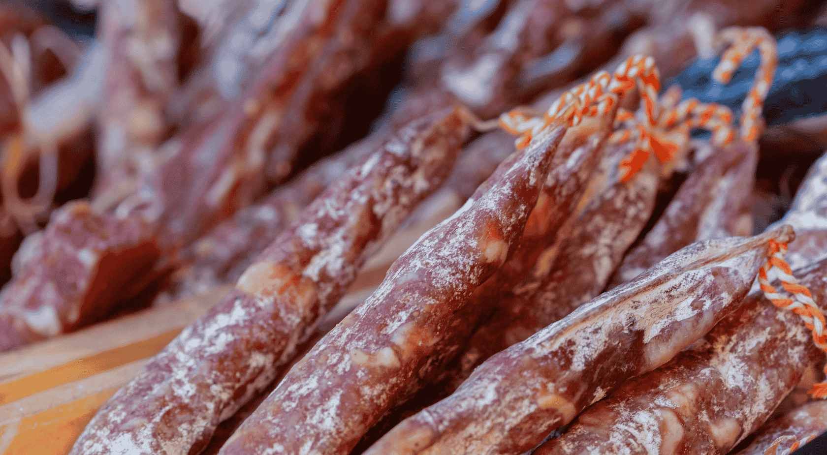 Primer plano de embutidos curados, cubiertos de moho blanco, atados con hilo rojo.