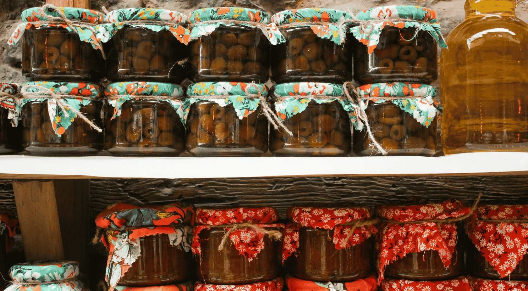 En los estantes se exhiben frascos de conservas: las filas superiores están cubiertas con tela verde oliva; las inferiores, con tapas estampadas en rojo.