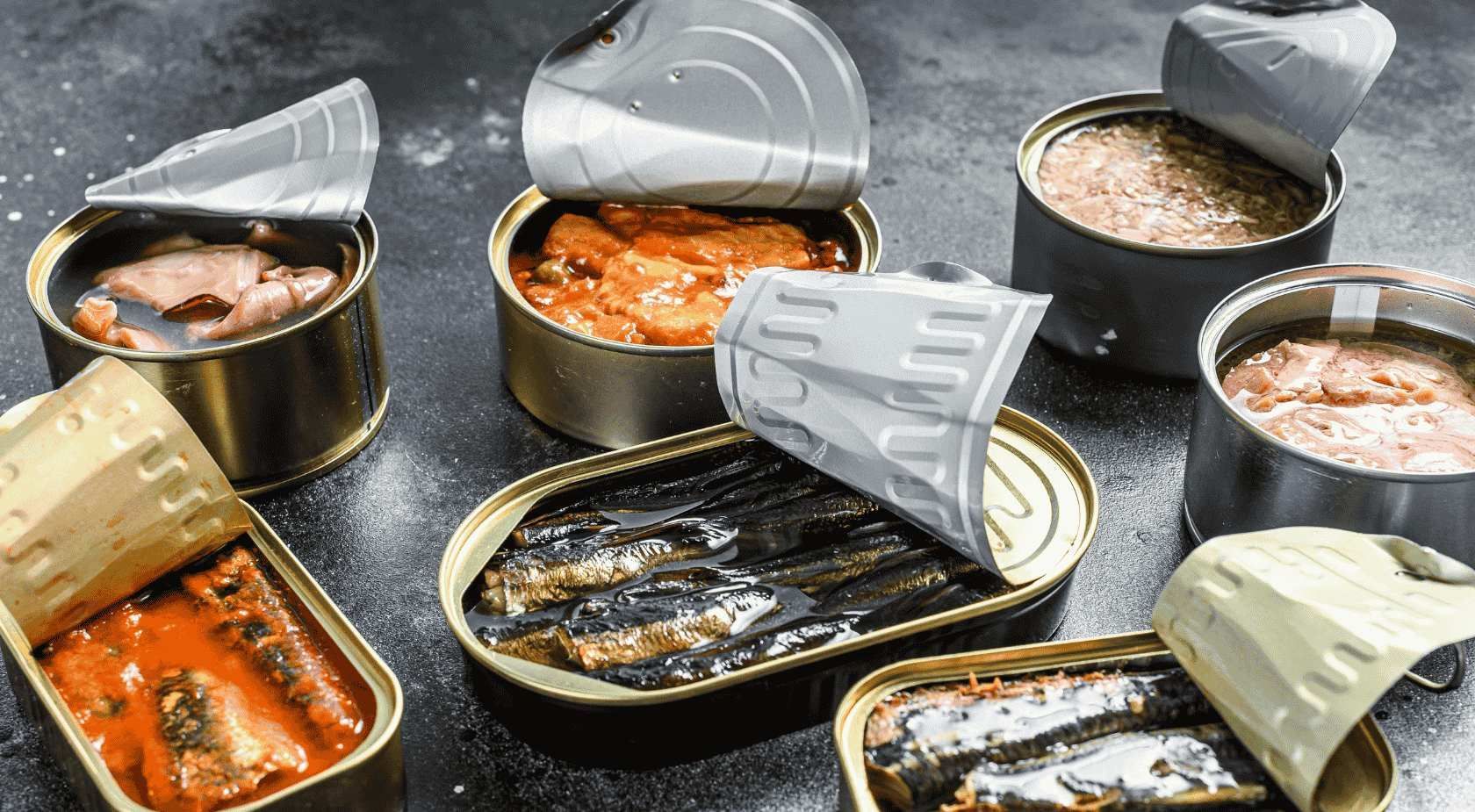 Latas abiertas de diversos alimentos en conserva sobre una superficie oscura, incluyendo pescado y salsas.