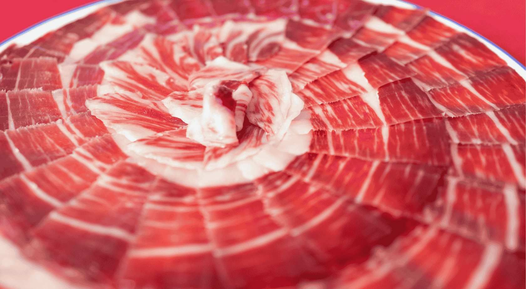Jamón español cortado en finas lonchas y dispuesto en espiral sobre un plato blanco.