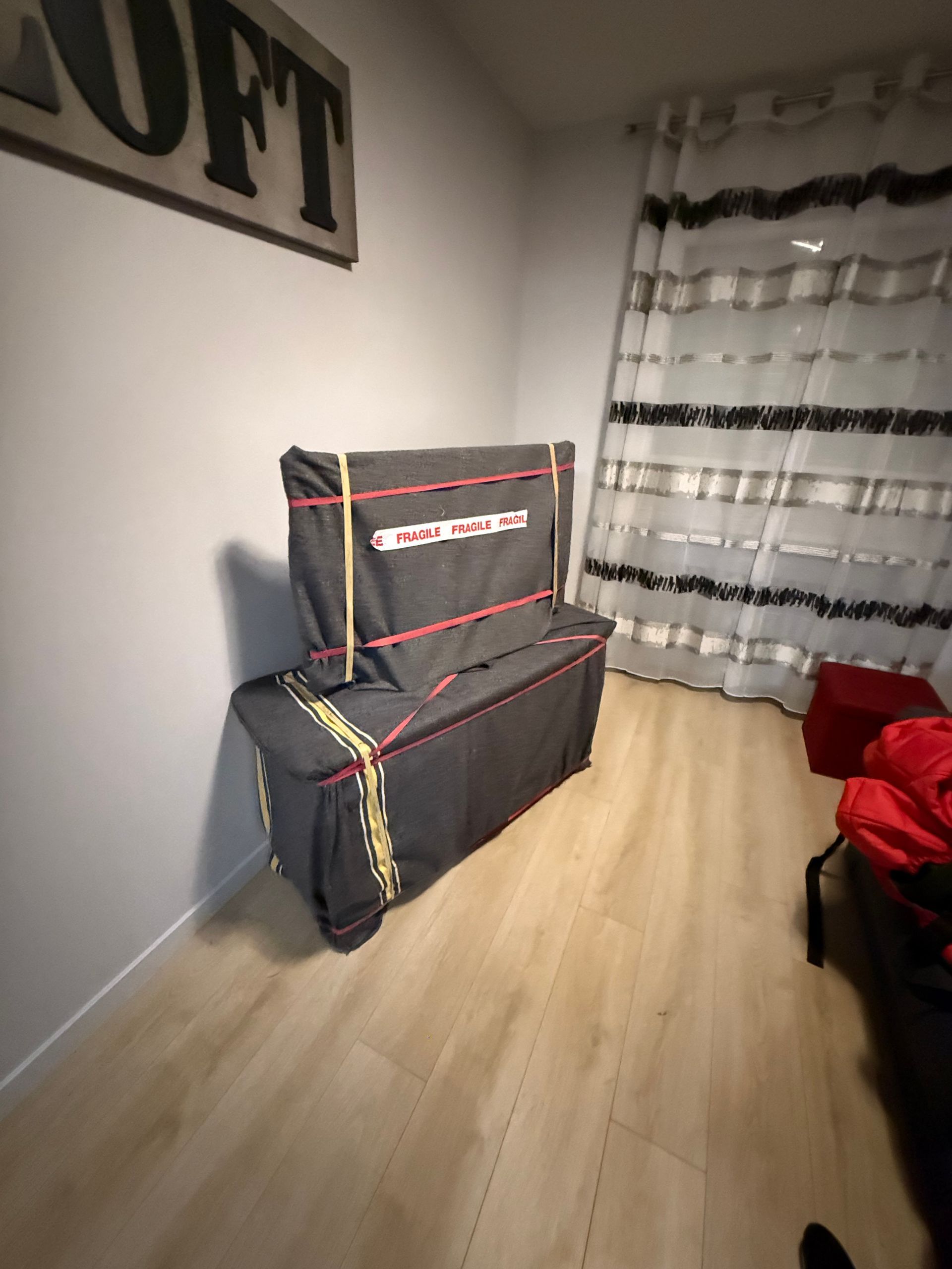 Paquets emballés et recouverts de sangles rouges et jaunes qui se trouvent dans une pièce avec un rideau et un sol en bois