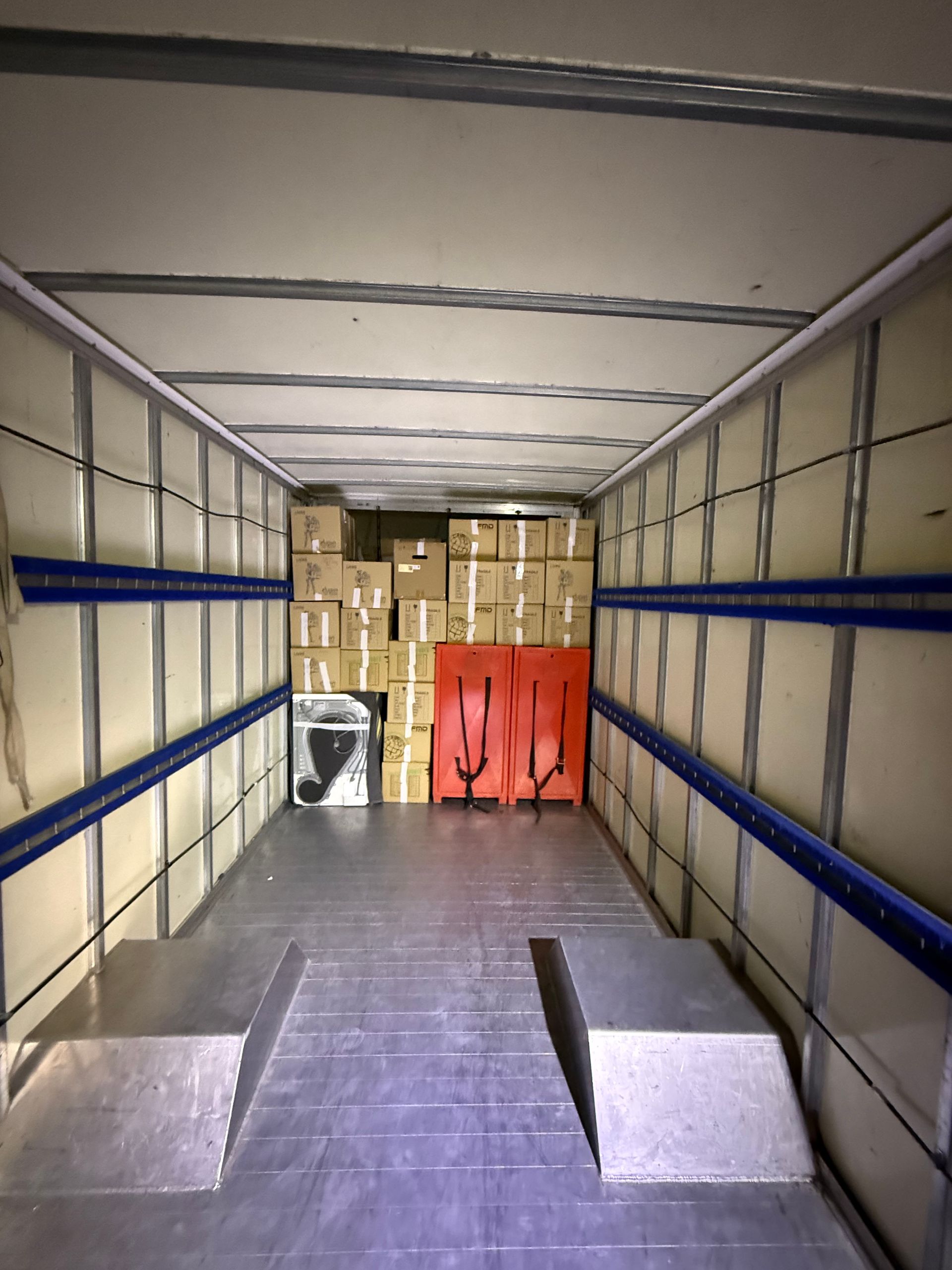 Intérieur d'une semi-remorque chargée de cartons, de deux équipements de sécurité orange et d'une plateforme métallique