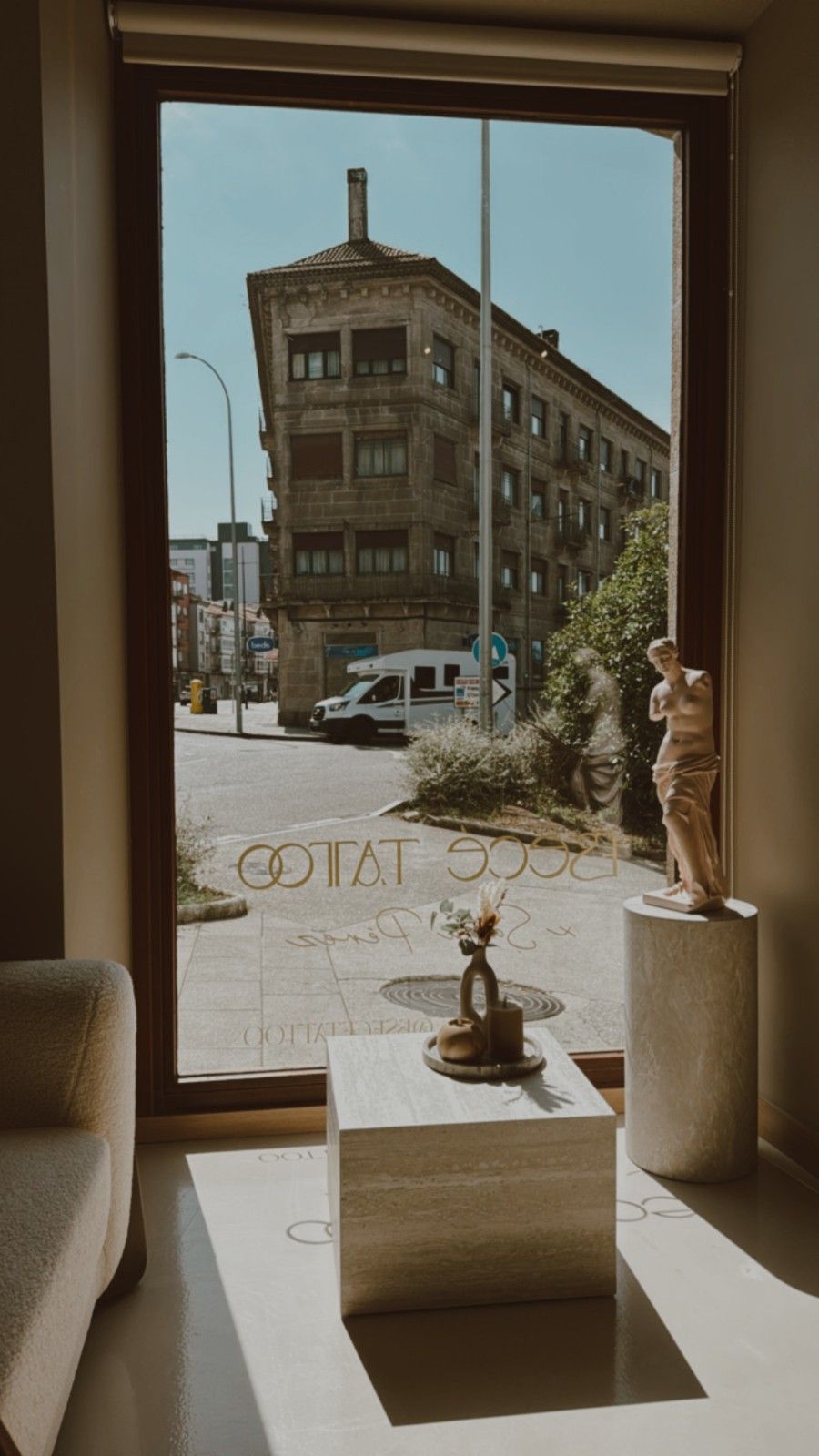 Vista de una calle de la ciudad desde una ventana, con un edificio, estatuas, una mesa y un automóvil.