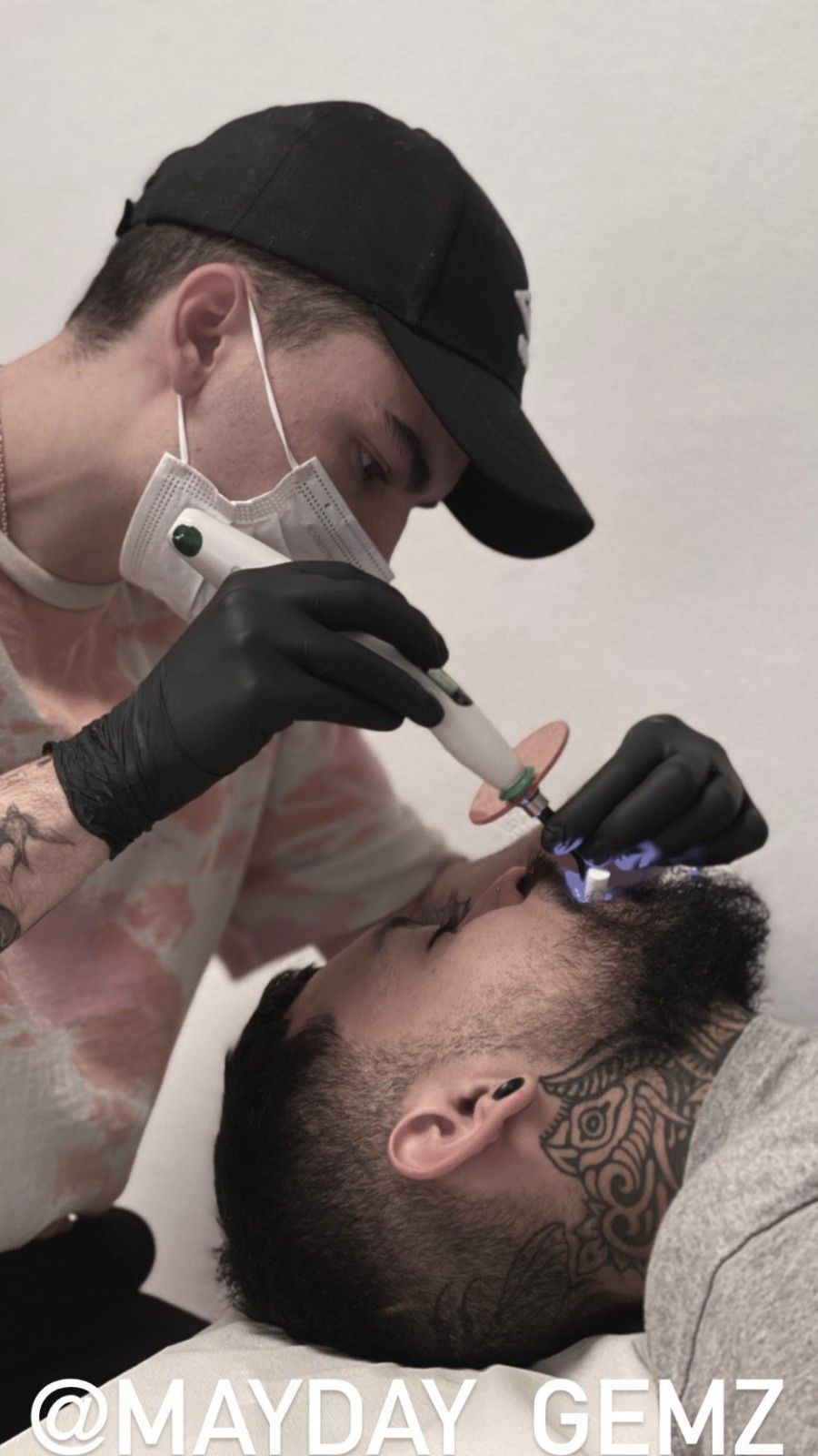Una persona recibe una gema dental por parte de un técnico enmascarado. El rostro de la persona está en primer plano; un dispositivo apunta a sus dientes.