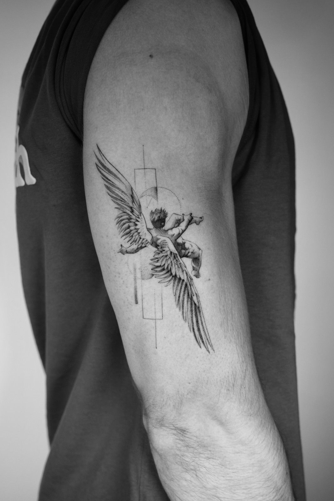 Tatuaje en blanco y negro de un ángel con alas en la parte superior del brazo de una persona.