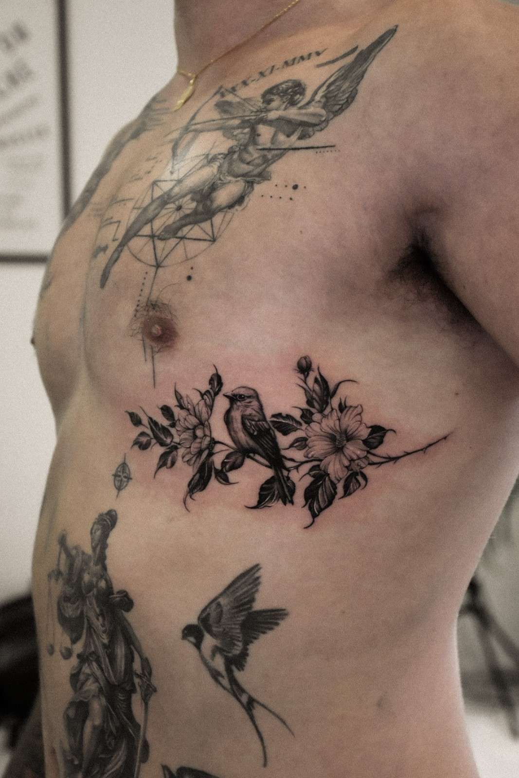 Tatuaje en el torso. Incluye un ángel, flores, pájaros y otras figuras.