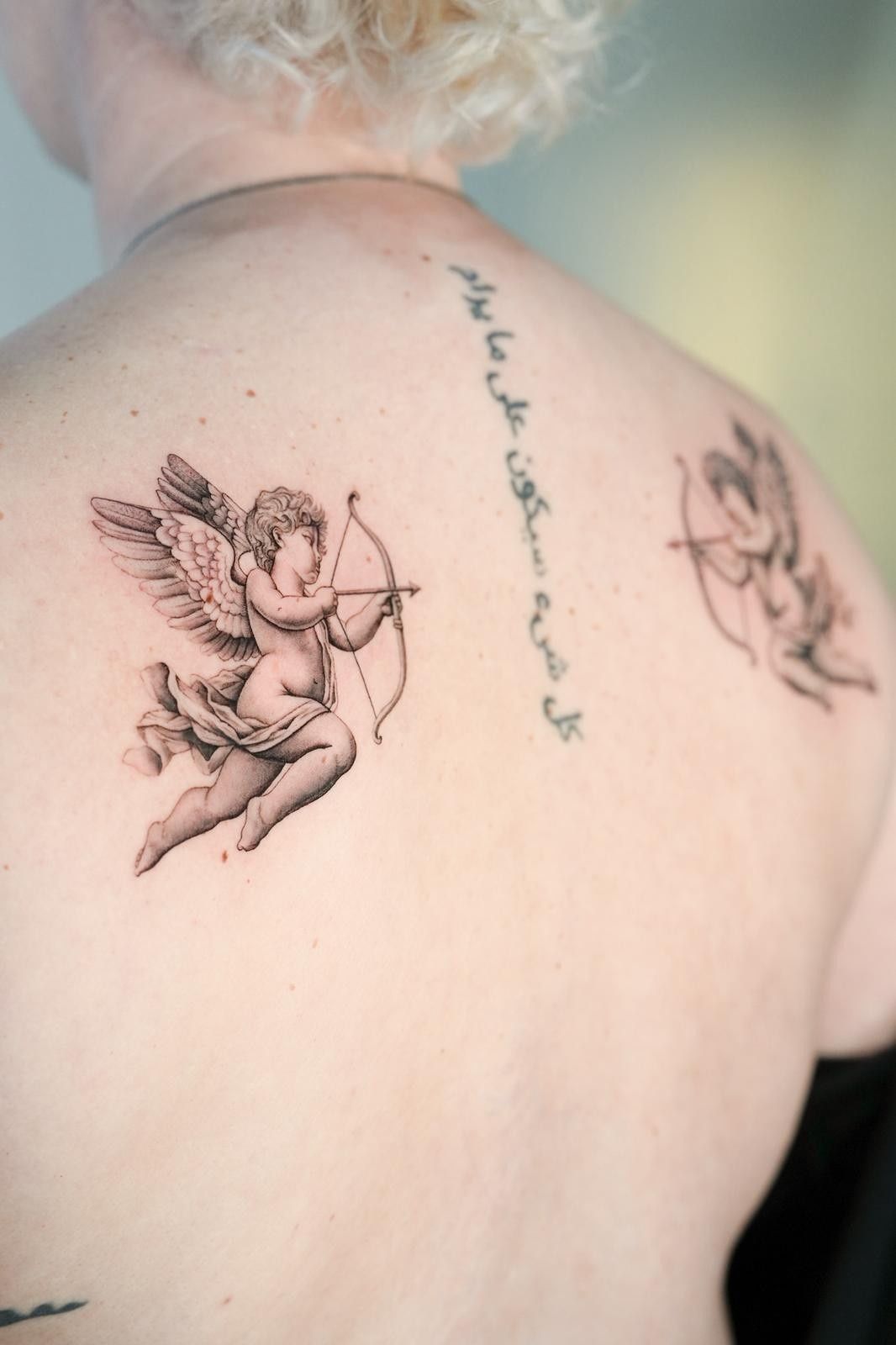 Tatuaje en la espalda: Cupido con arco y flecha, contorno de ángel, escritura árabe.