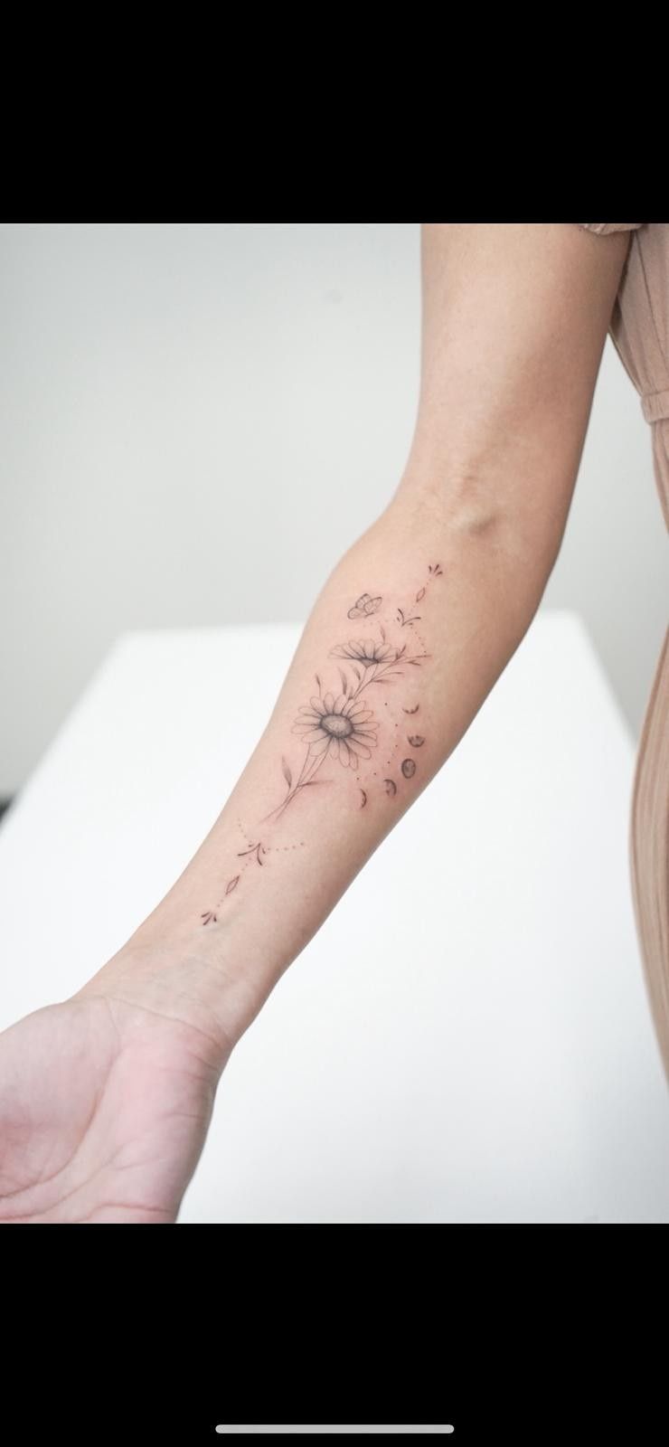 Un tatuaje de diente de león en el antebrazo de una persona, con semillas volando.