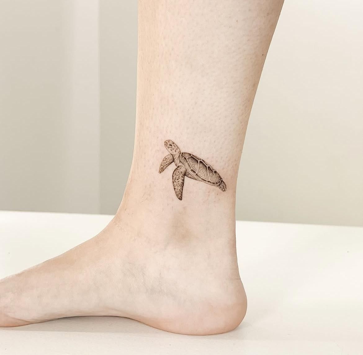 Tobillo con un pequeño tatuaje de una tortuga marina en tinta negra.