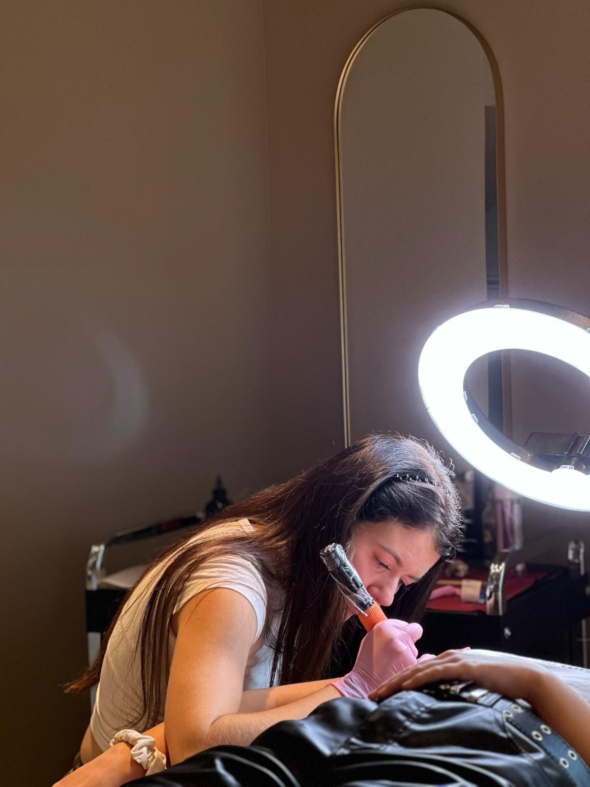 Mujer realizando un procedimiento cosmético con una herramienta similar a un bolígrafo sobre la piel de una persona, iluminada por un anillo de luz.