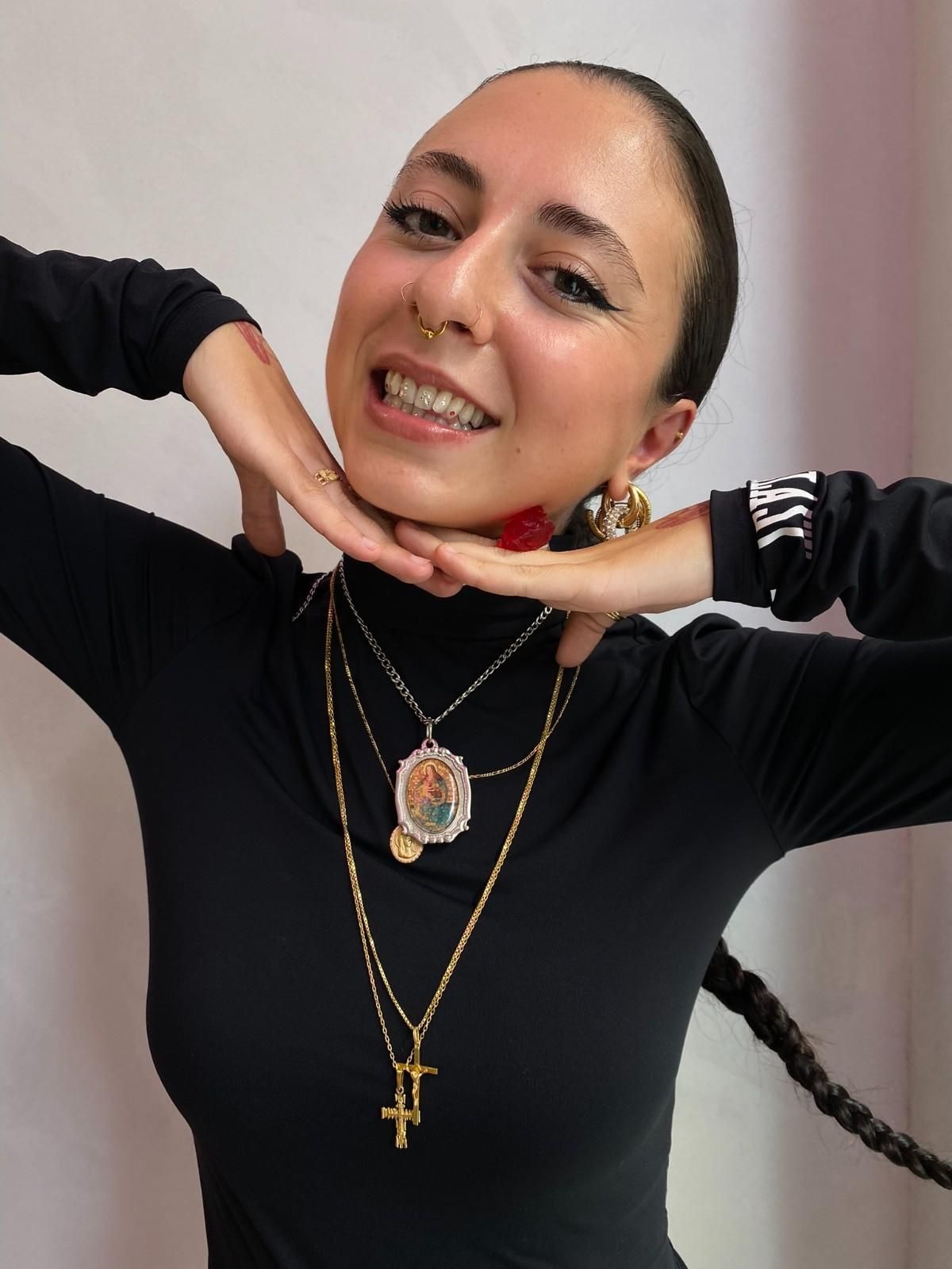 Mujer con gemas dentales y piercings, sonriendo, con las manos cerca de la cara.