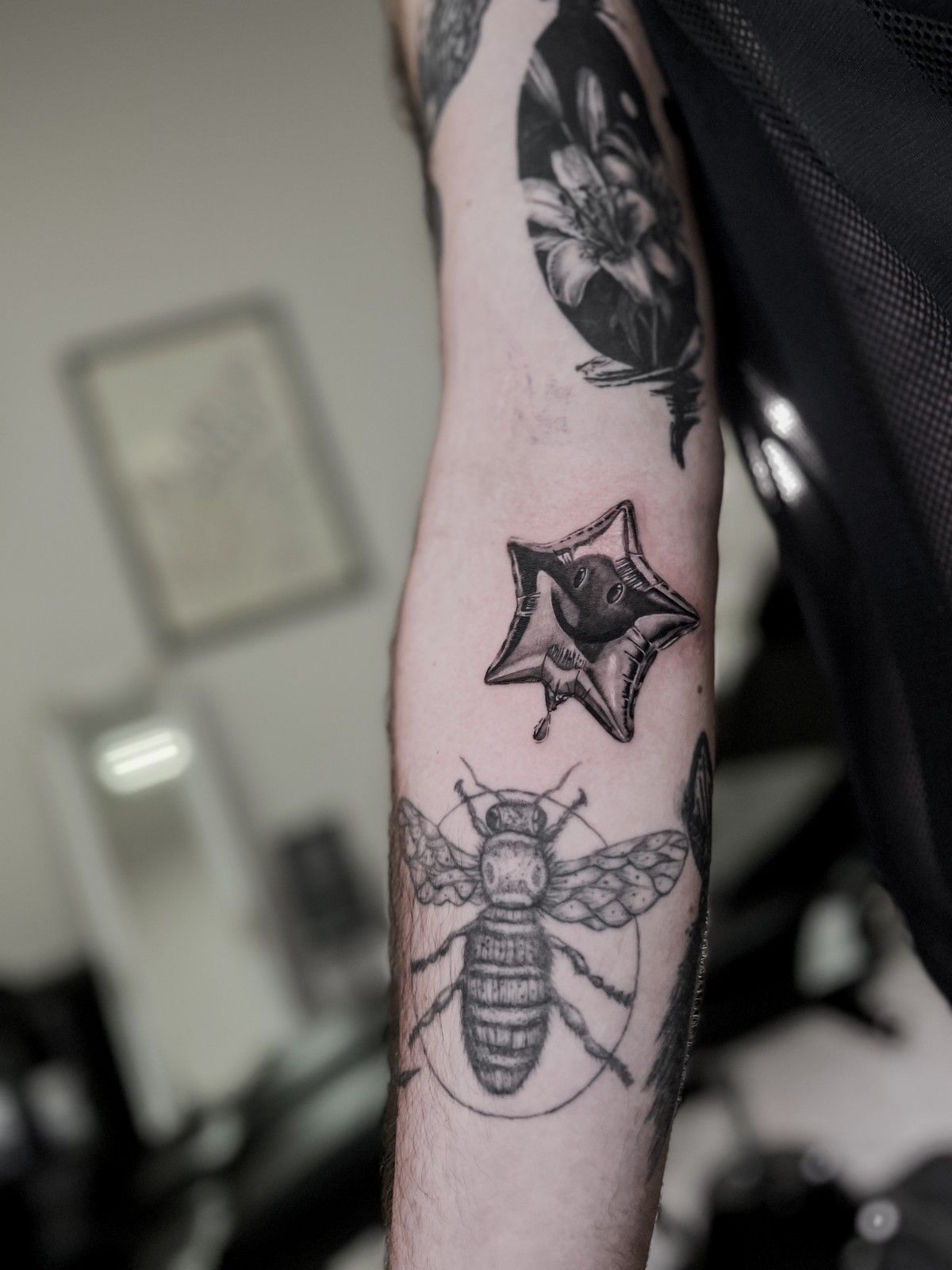 Tatuaje de una abeja, un globo desinflado en forma de estrella y una flor en un brazo.