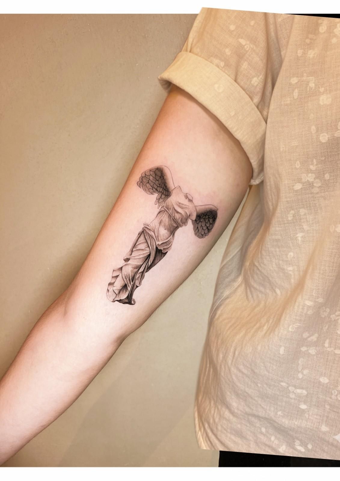 Tatuaje de la escultura de la Victoria Alada de Samotracia en el brazo de una persona.