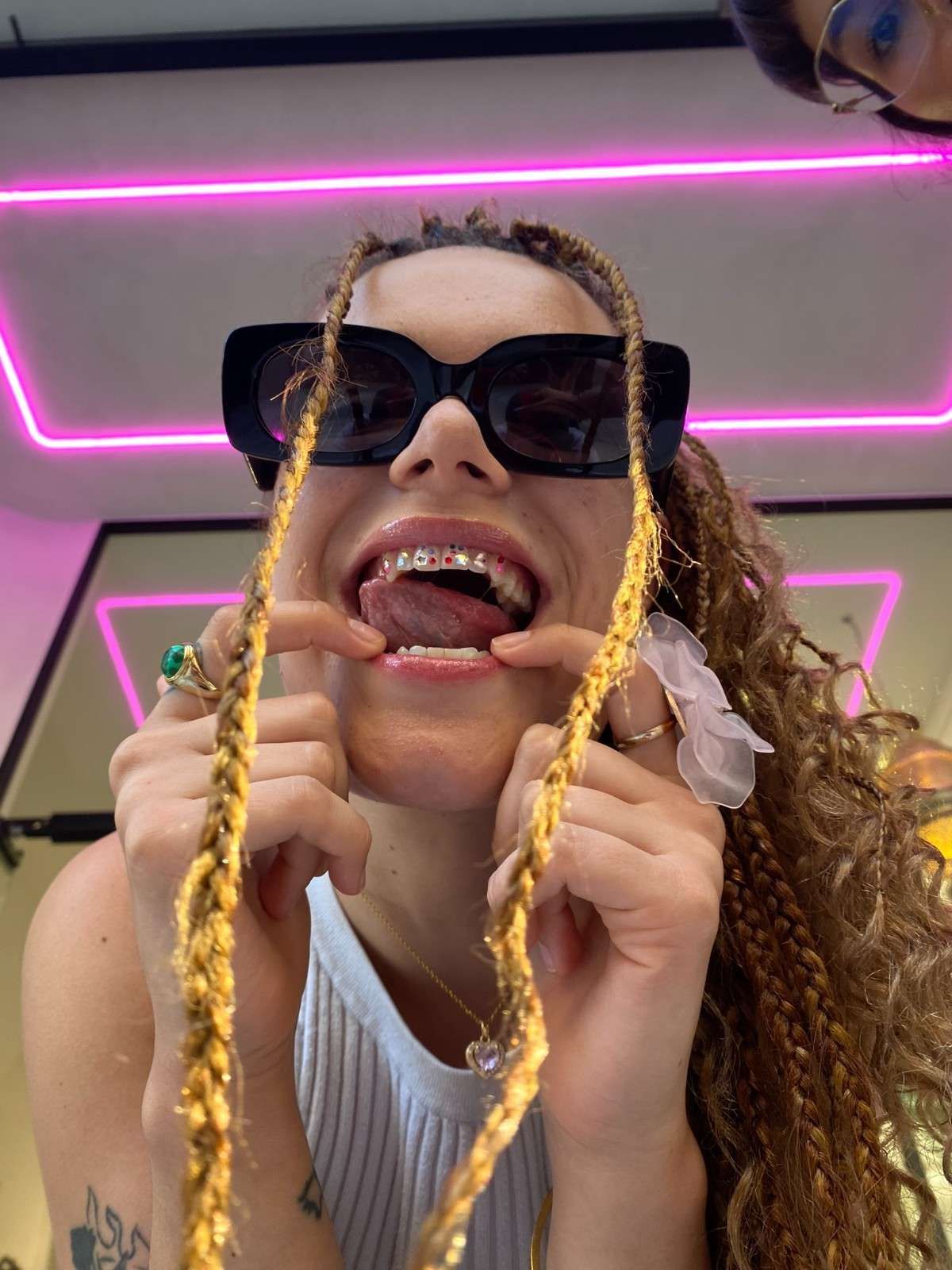 Persona con gafas de sol, sonriendo, tirando de trenzas, con gemas dentales.