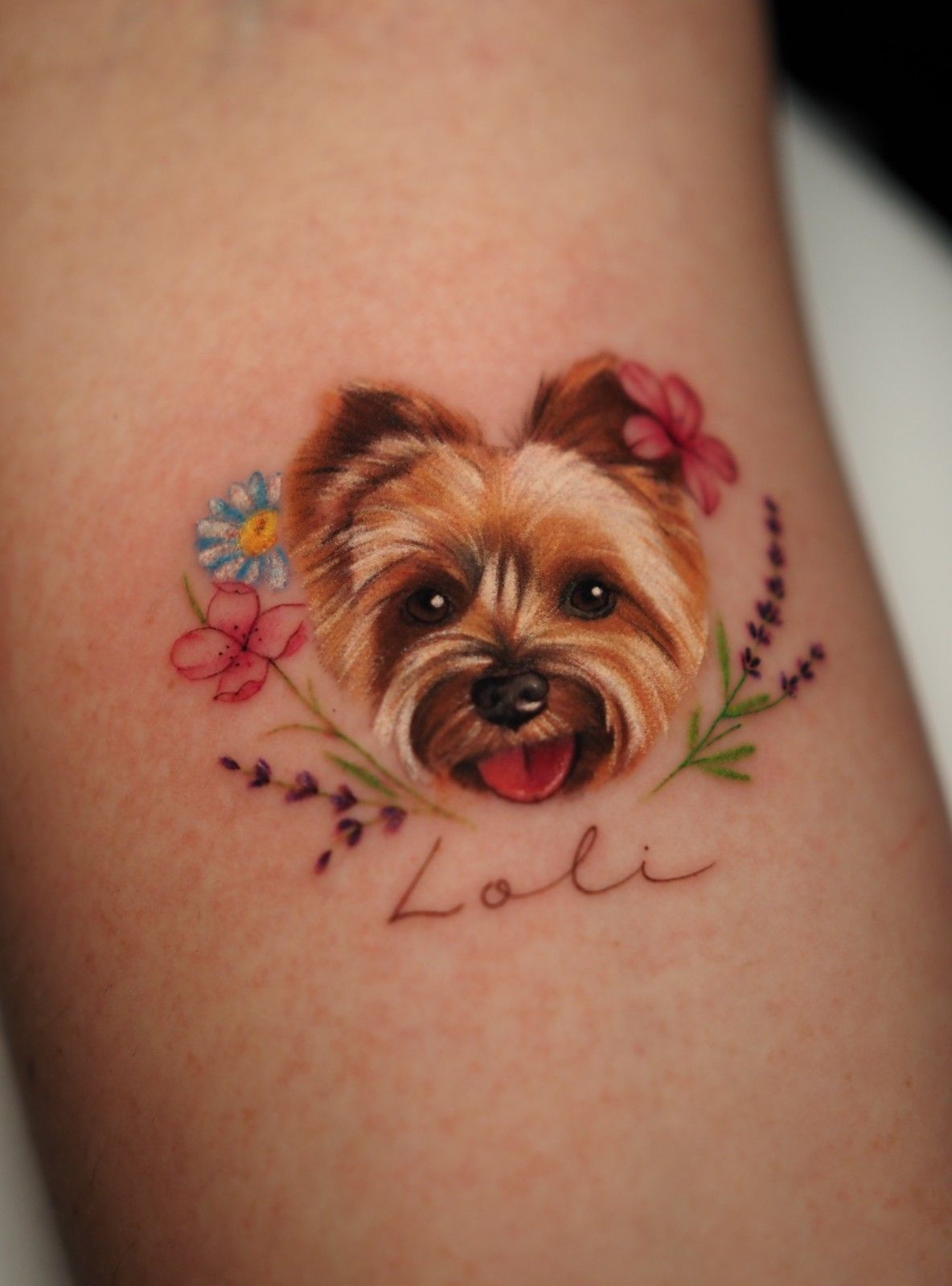 Tatuaje de un Yorkshire Terrier sonriente rodeado de flores, el nombre 