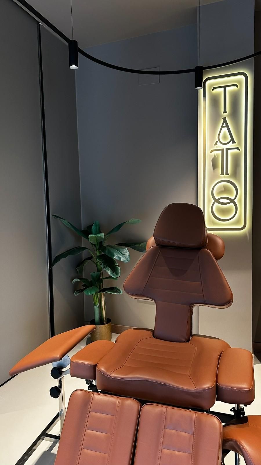 Silla de tatuaje en un estudio, de cuero marrón. Letrero de neón 