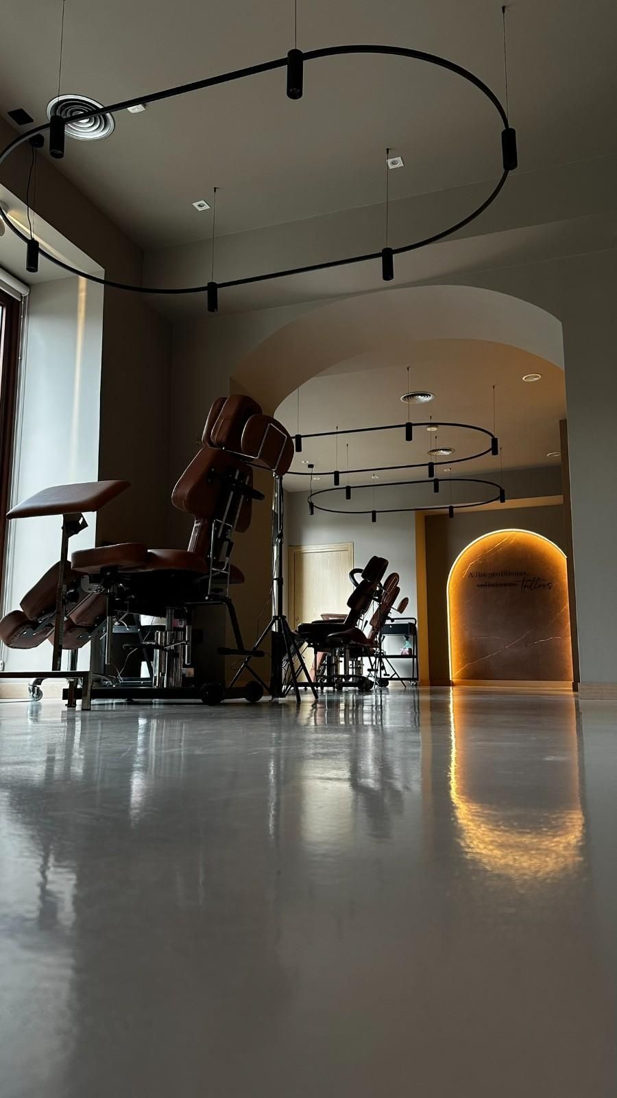 Habitación moderna y luminosa con dos sillones de masaje, iluminación de riel curva y una puerta arqueada brillante.