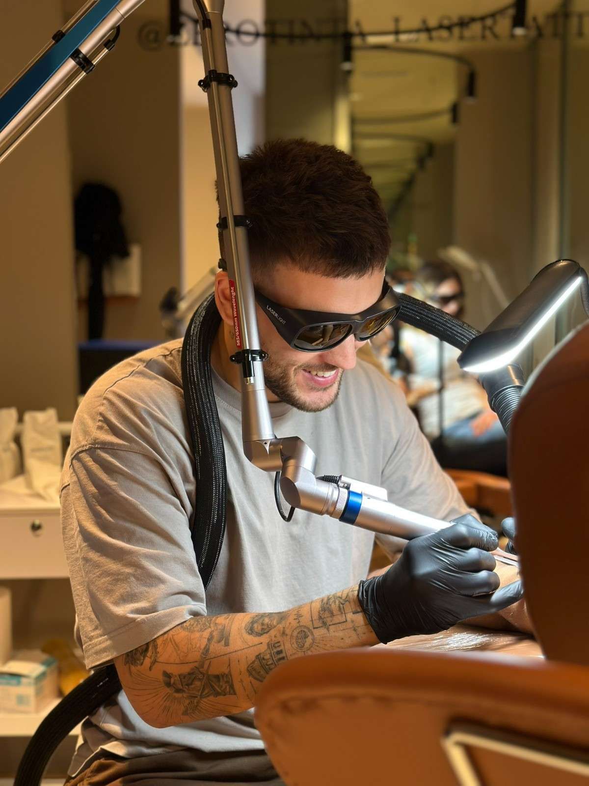 Hombre operando un dispositivo láser, usando gafas y guantes protectores, eliminando tatuajes.