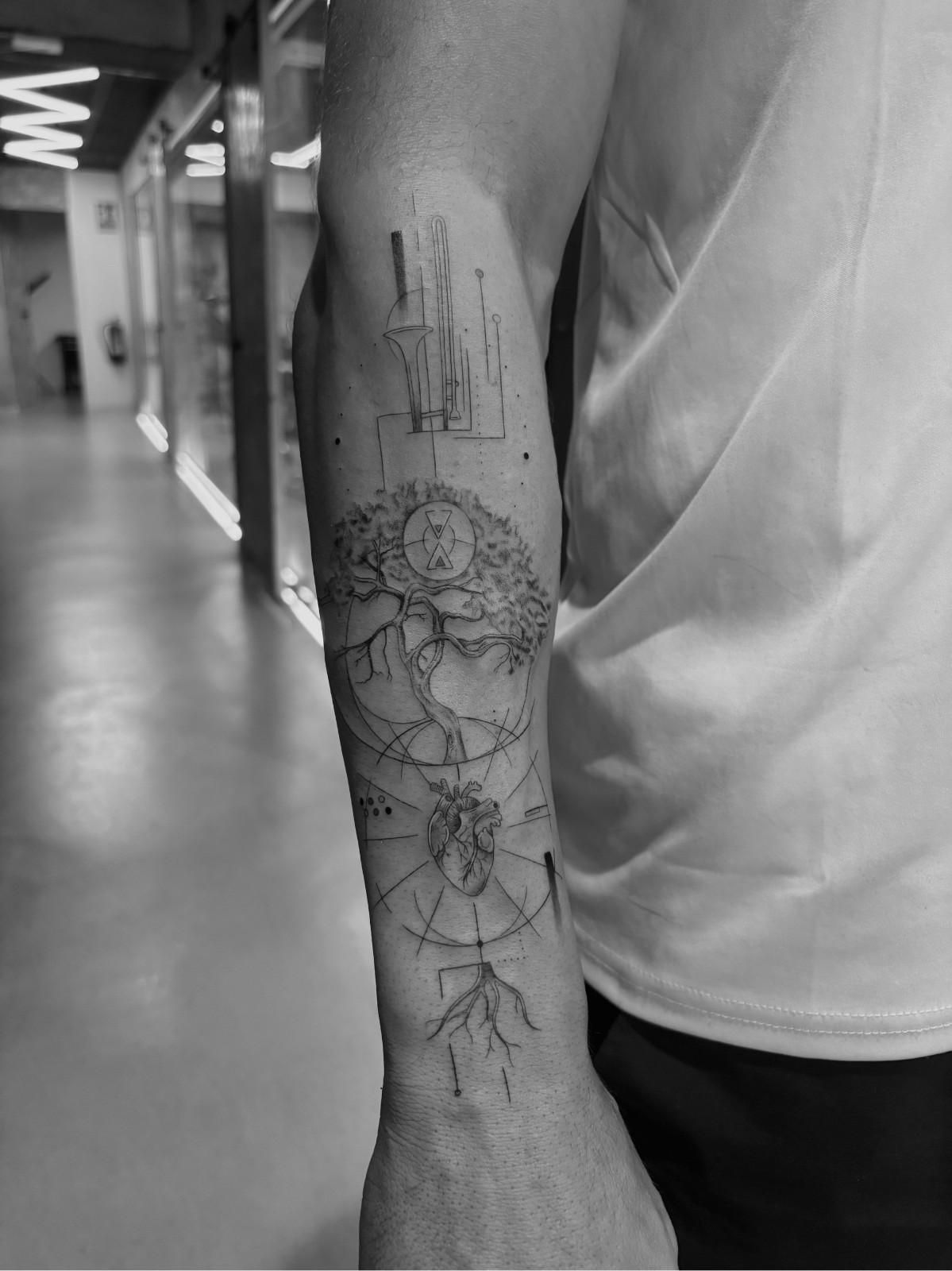 Tatuaje en blanco y negro de un árbol en el antebrazo de una persona, con raíces y ramas.